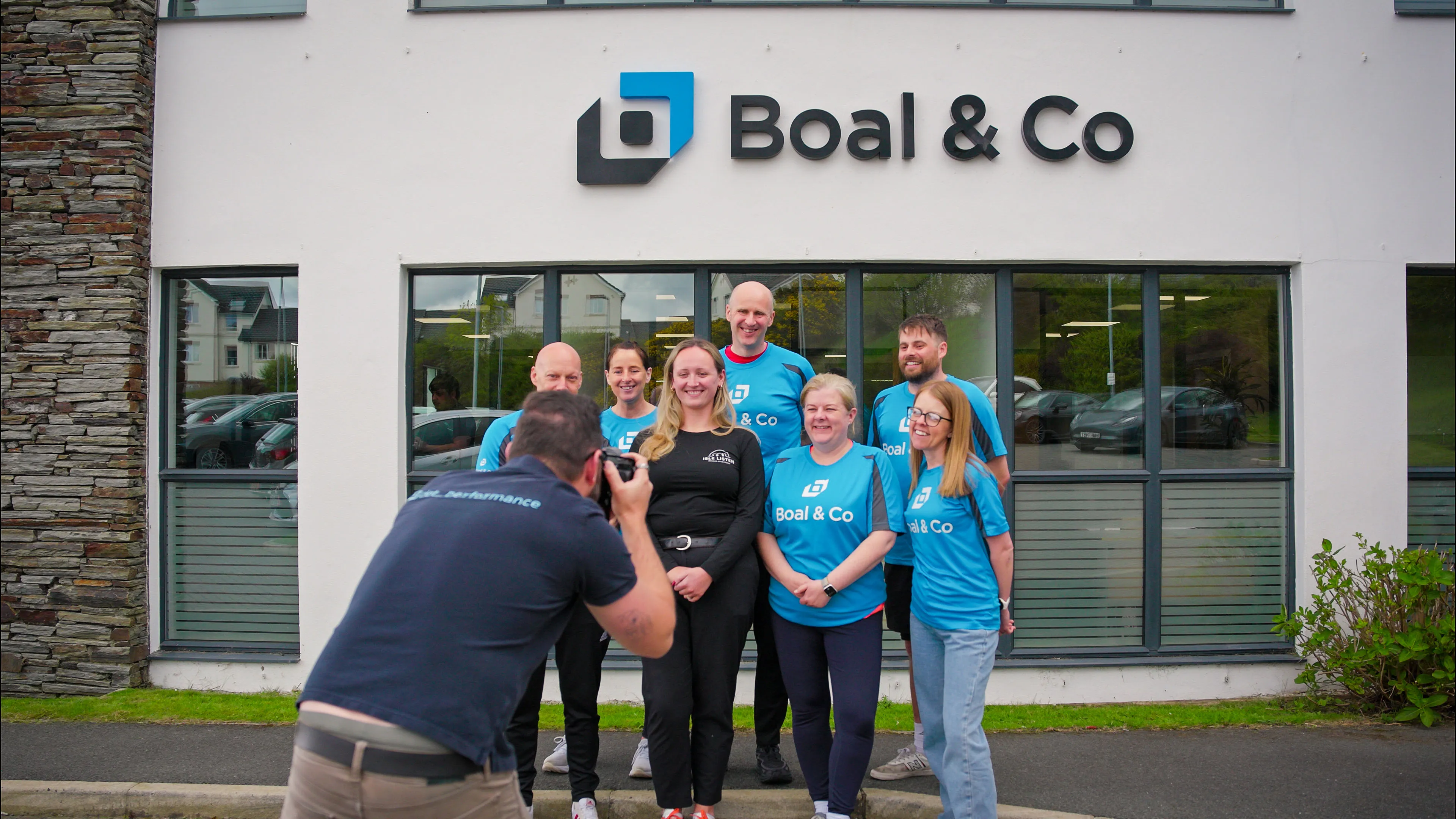 Nico van Loggerenberg from DotPerformance photographing Greg Collins, Karen McHale,James Bassett, Christine Evans, Andrew Cover, Vicky Mackie alongside Jess Knight from Isle Listen outside the Boal & Co office in Douglas, Isle of Man