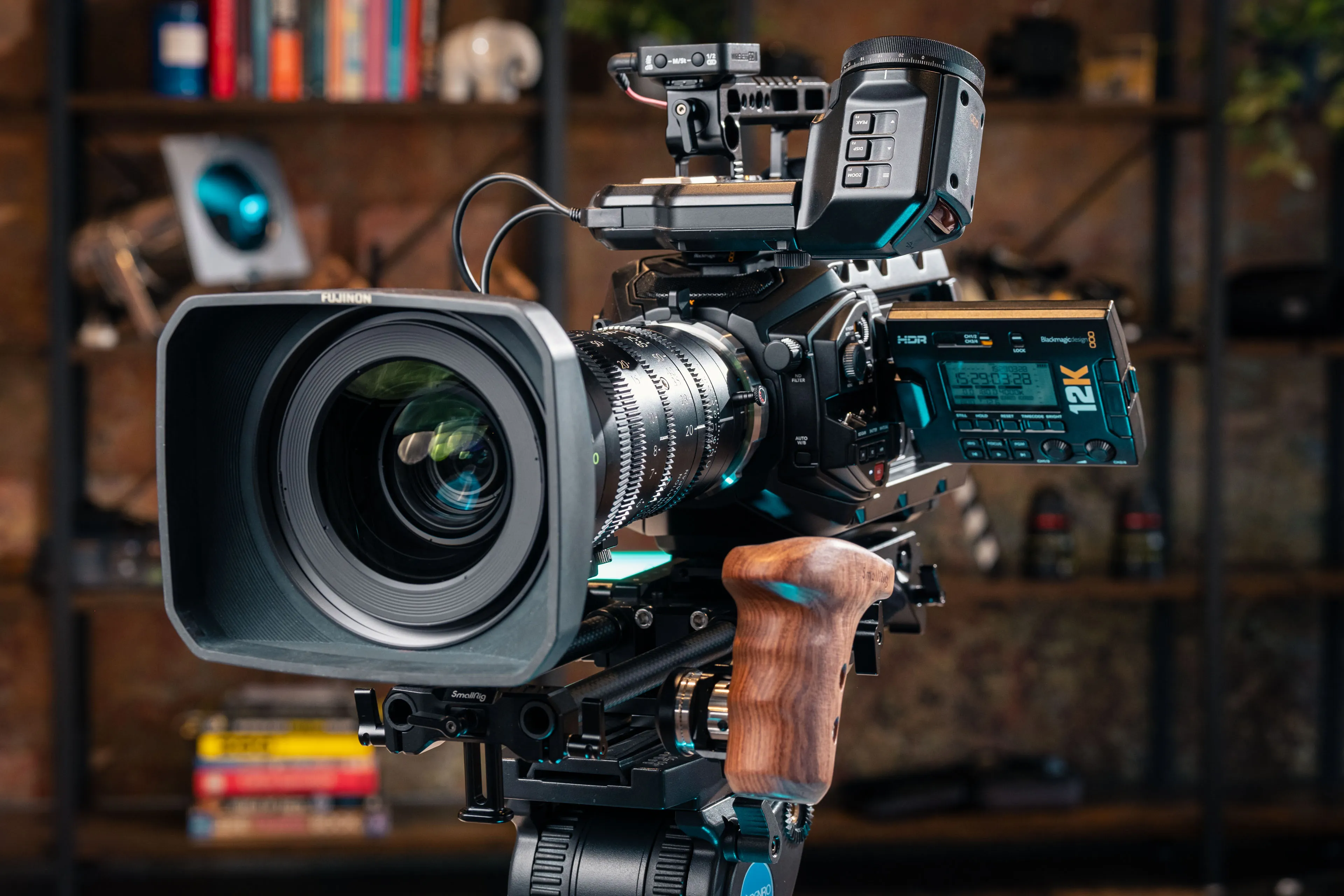 A professional video camera with a large lens, digital controls, and a wooden grip, set against a stylish backdrop of books and decor.