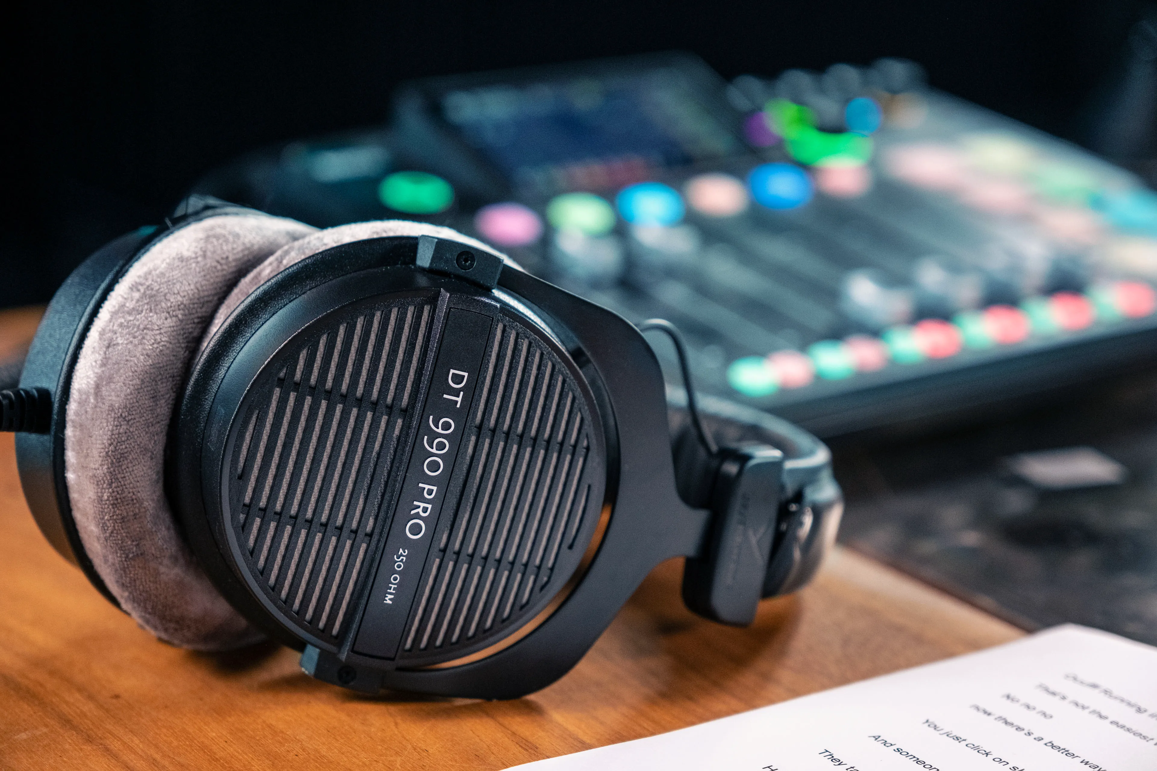 Close-up of DT 990 Pro headphones resting on a wooden surface beside a mixer and paperwork, showcasing their professional design.
