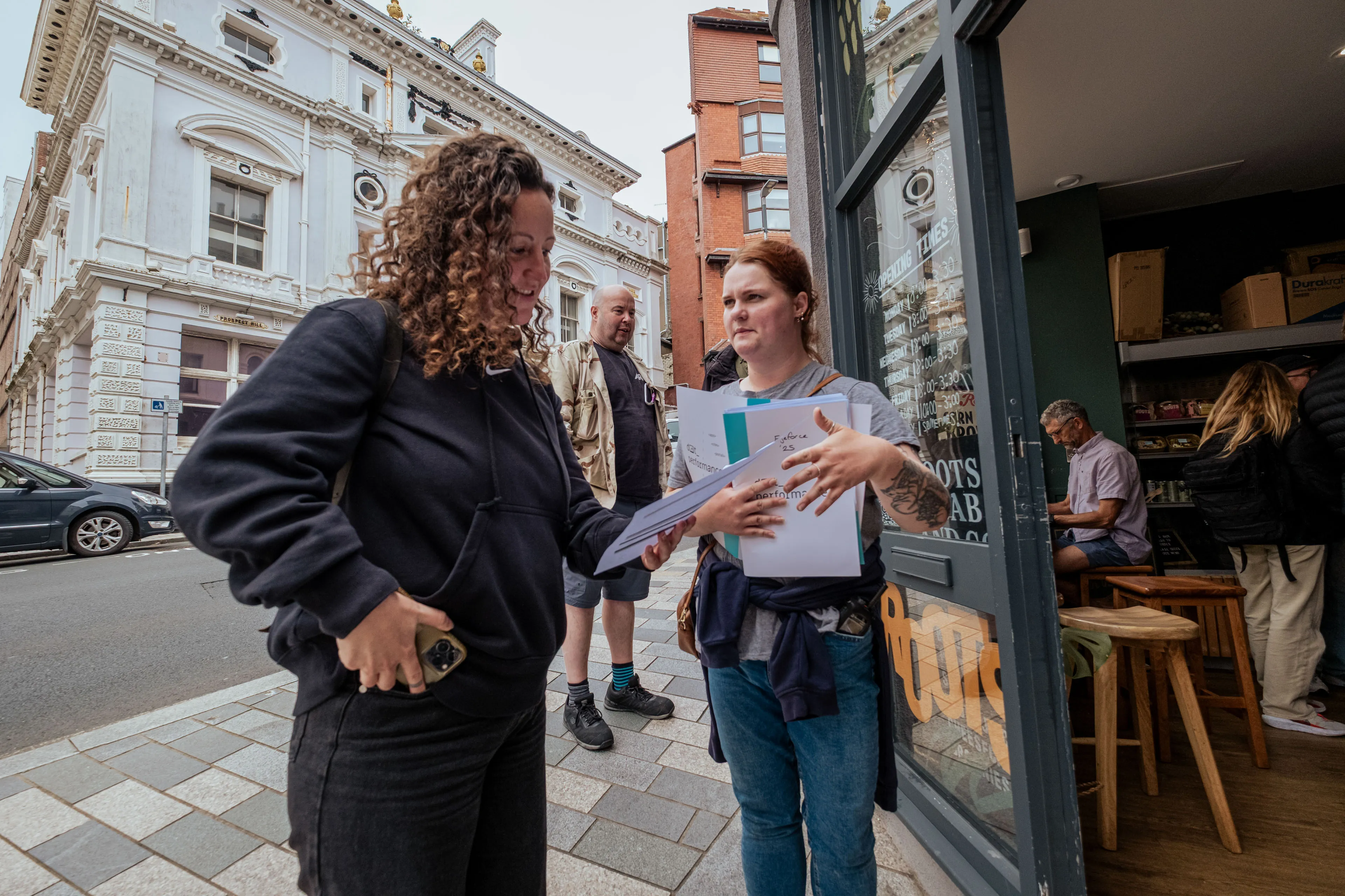 Paula Hamilton and Samantha Lowestand outside Roots cafe holding documents, preparing for the next shot,