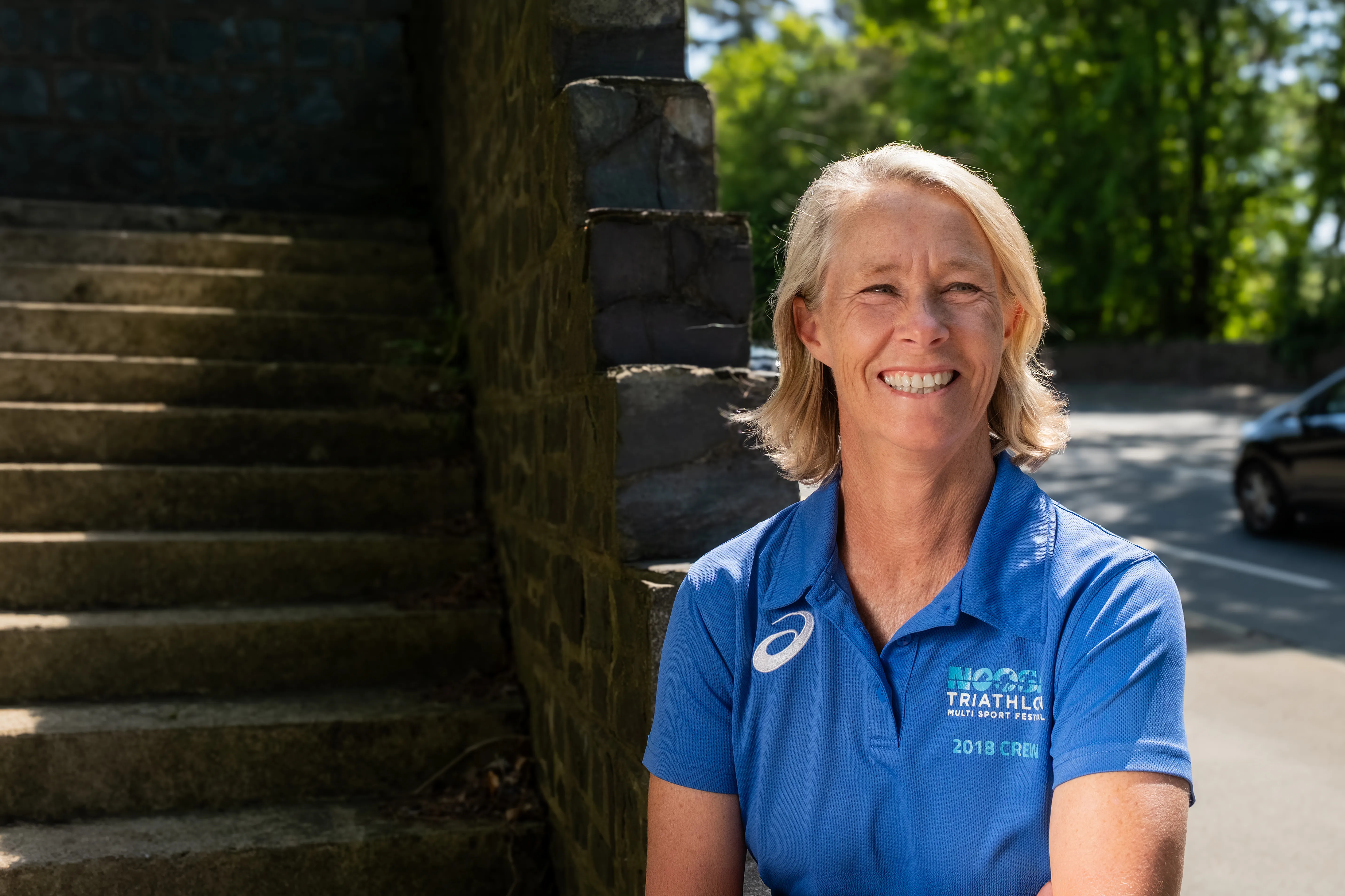 Robyn Entermann from Queensland, Australia, an Isle of Man TT Marshal, smiling outdoors for Behind the Tabard TT Marshals Series highlighting marshal stories, in a blue Noosa Triathlon polo shirt
