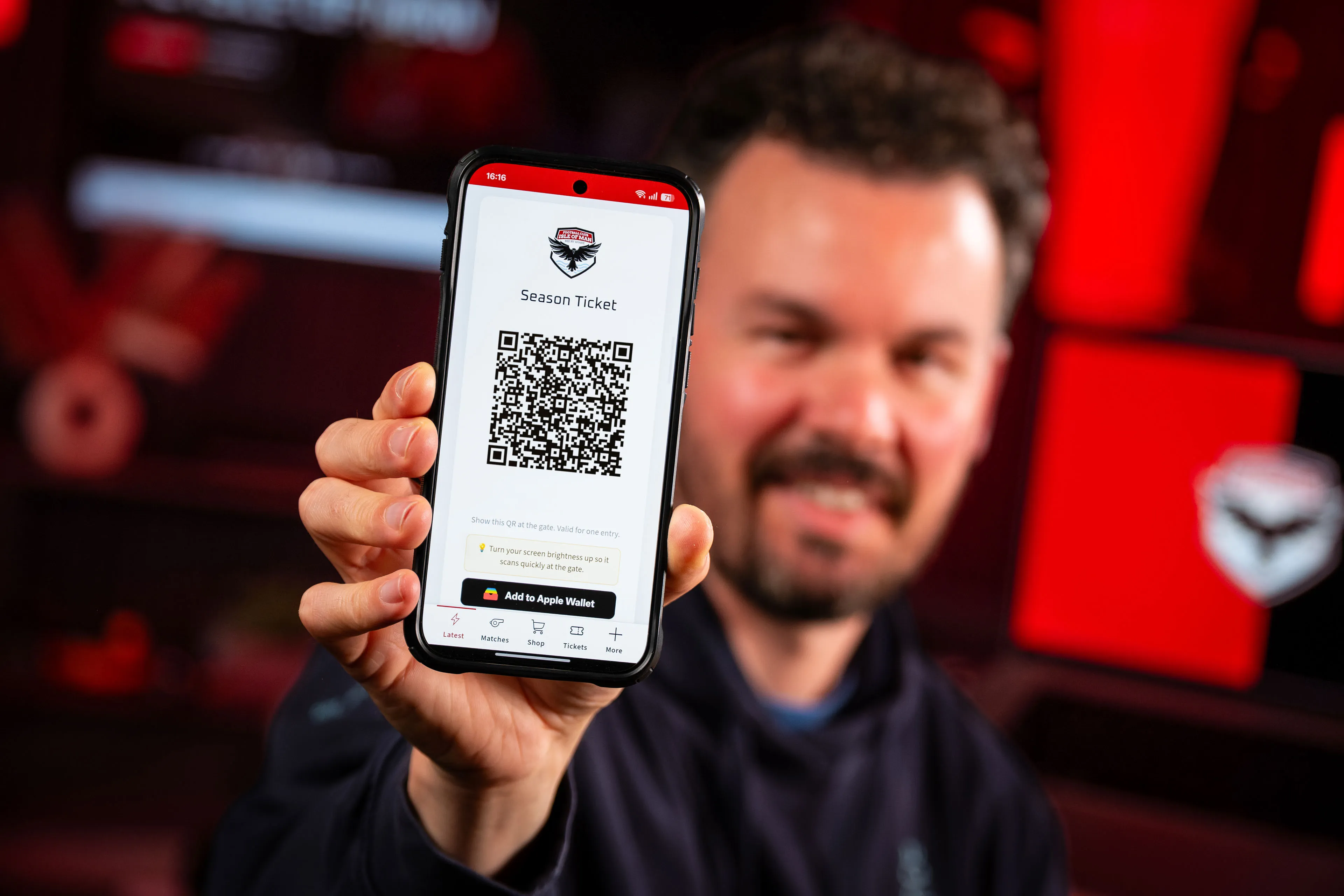 Adrian Crellin smiling and holding up his FCIOM season ticket QR code displayed on the club app