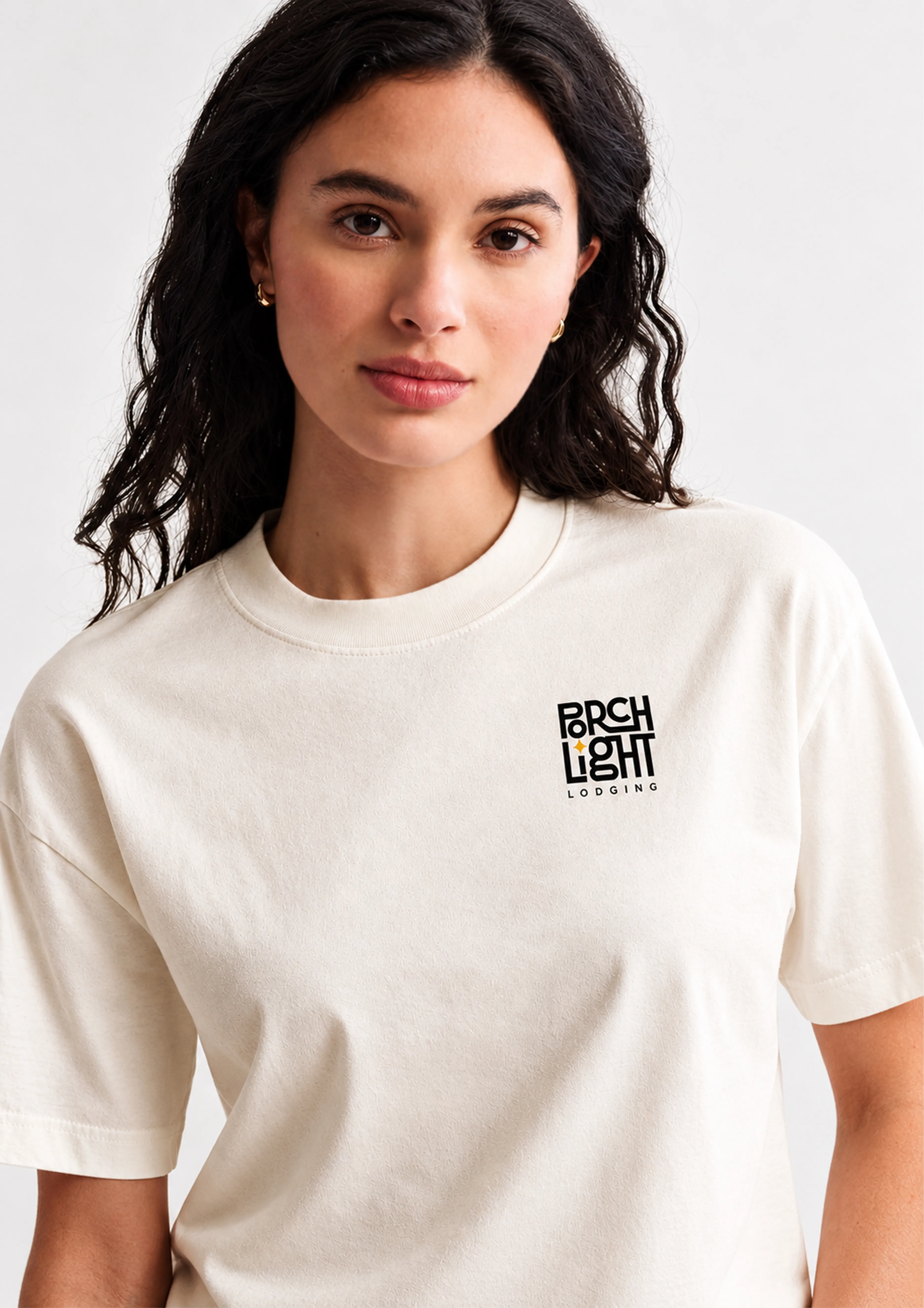 Woman with long dark hair wearing a cream PorchLight Lodging T-shirt with a small chest logo