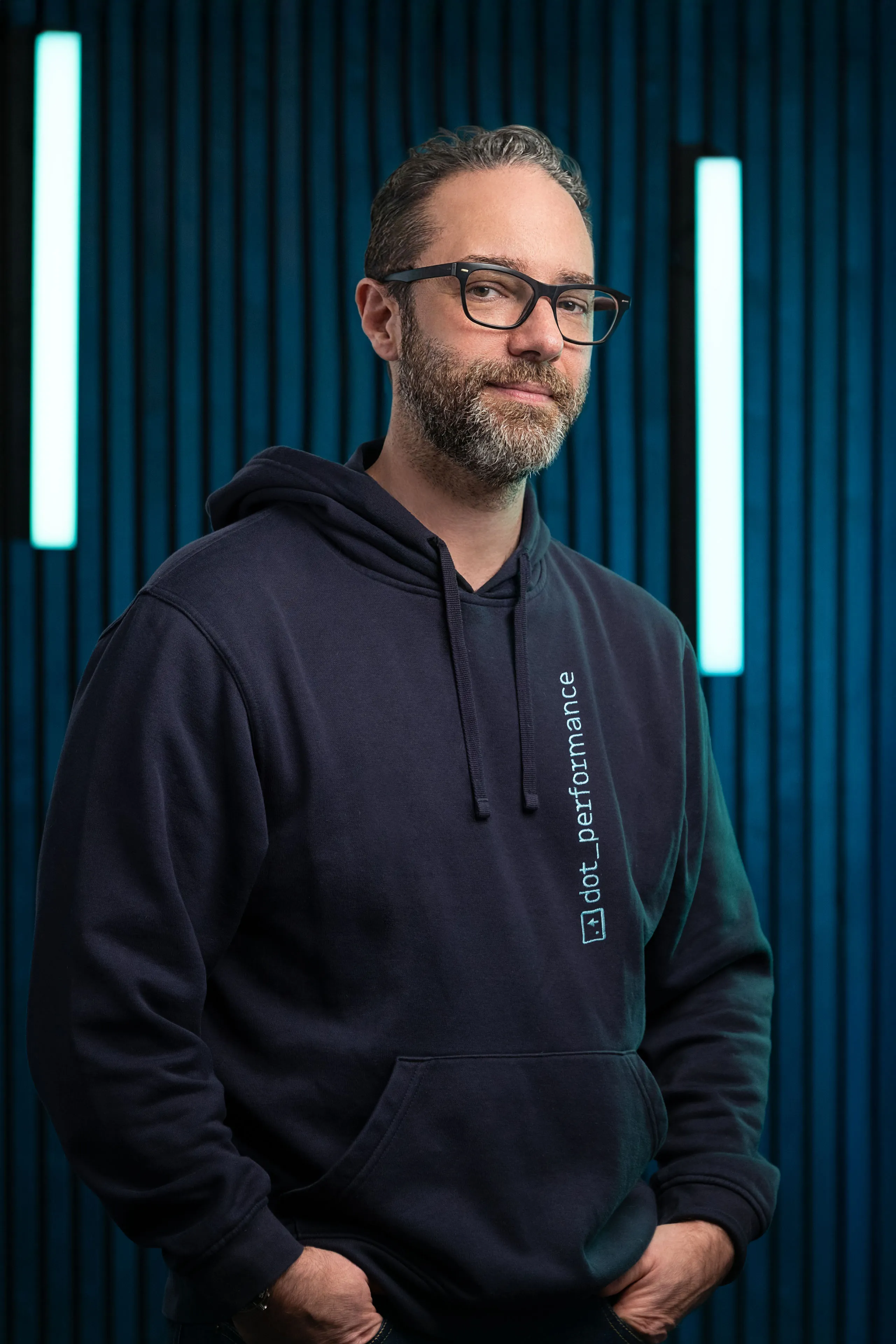 Theo Wiersma, Senior Developer at DotPerformance, photographed at DotPerformance studios on the Isle of Man, wearing a DotPerformance hoodie against a dark background with teal neon lighting