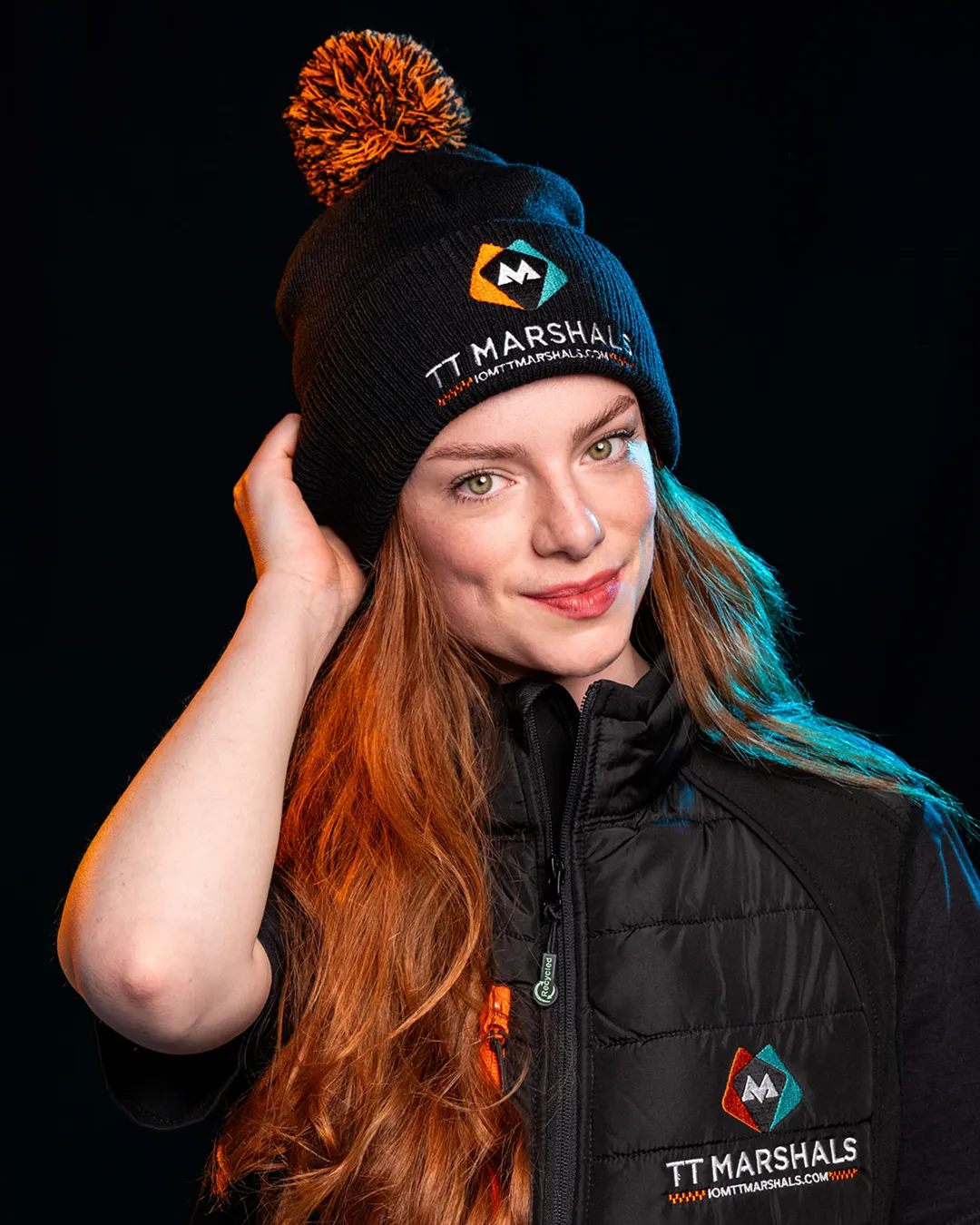 Ella Garvey wearing the official TT Marshals 2026 black bobble hat and gilet, featuring the TT Marshals logo. Exclusive marshal merchandise for the Isle of Man TT 2026.