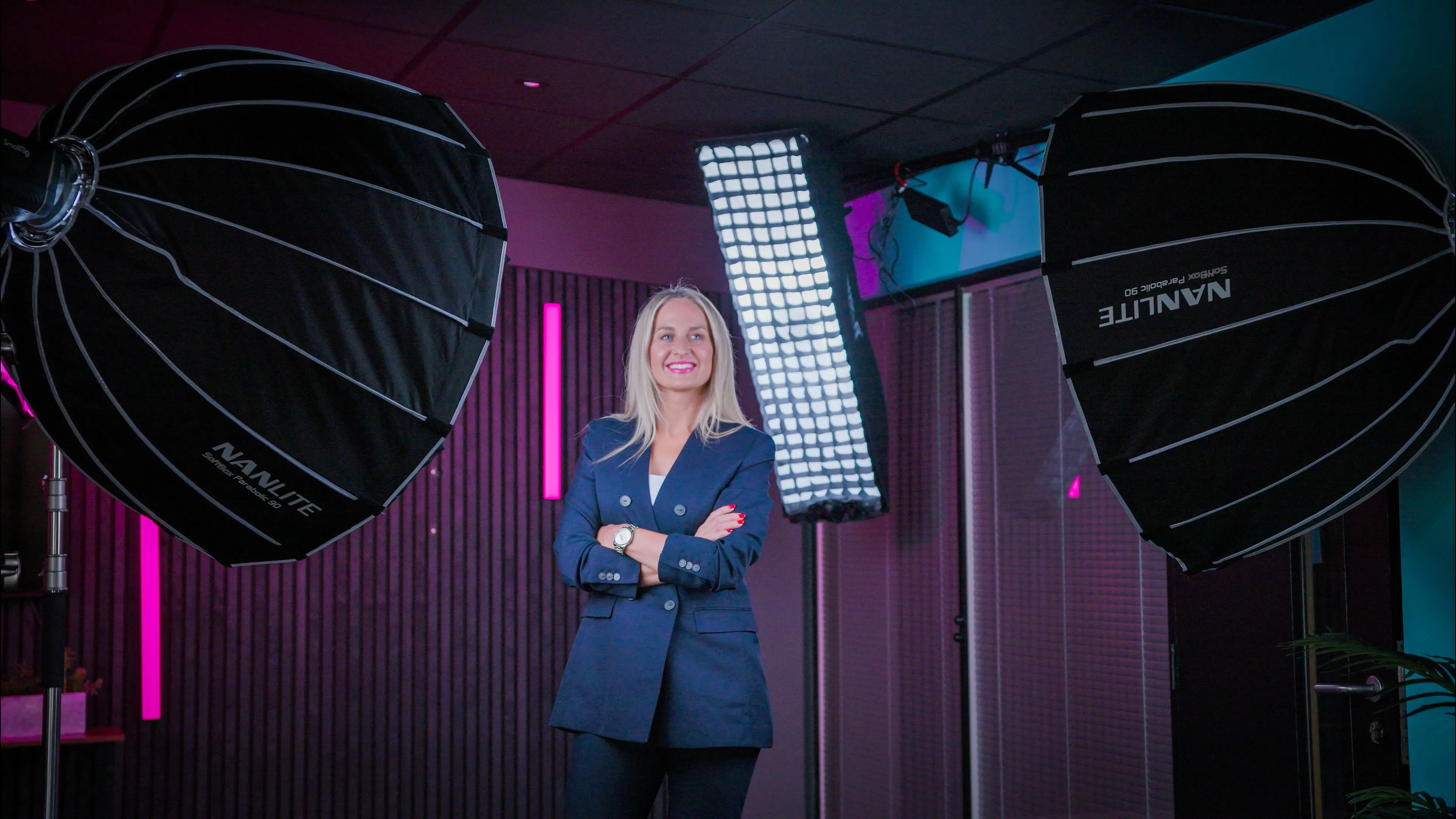 A woman in a dark blazer stands confidently in a professional studio setup with large lighting equipment. The mood is modern and dynamic.