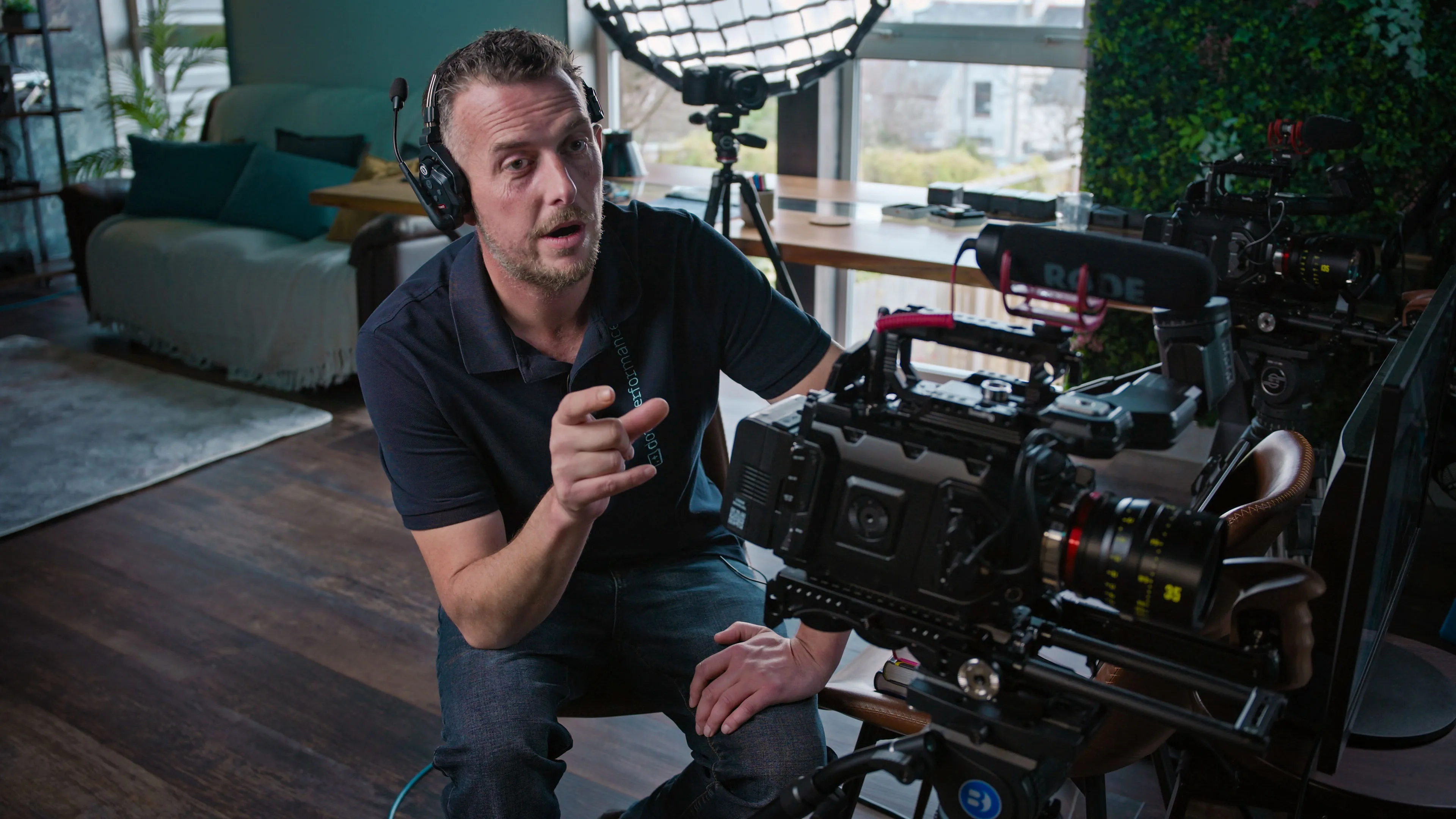 A person with headphones gestures towards a professional camera setup in a modern studio. The scene is focused and creative, conveying concentration.