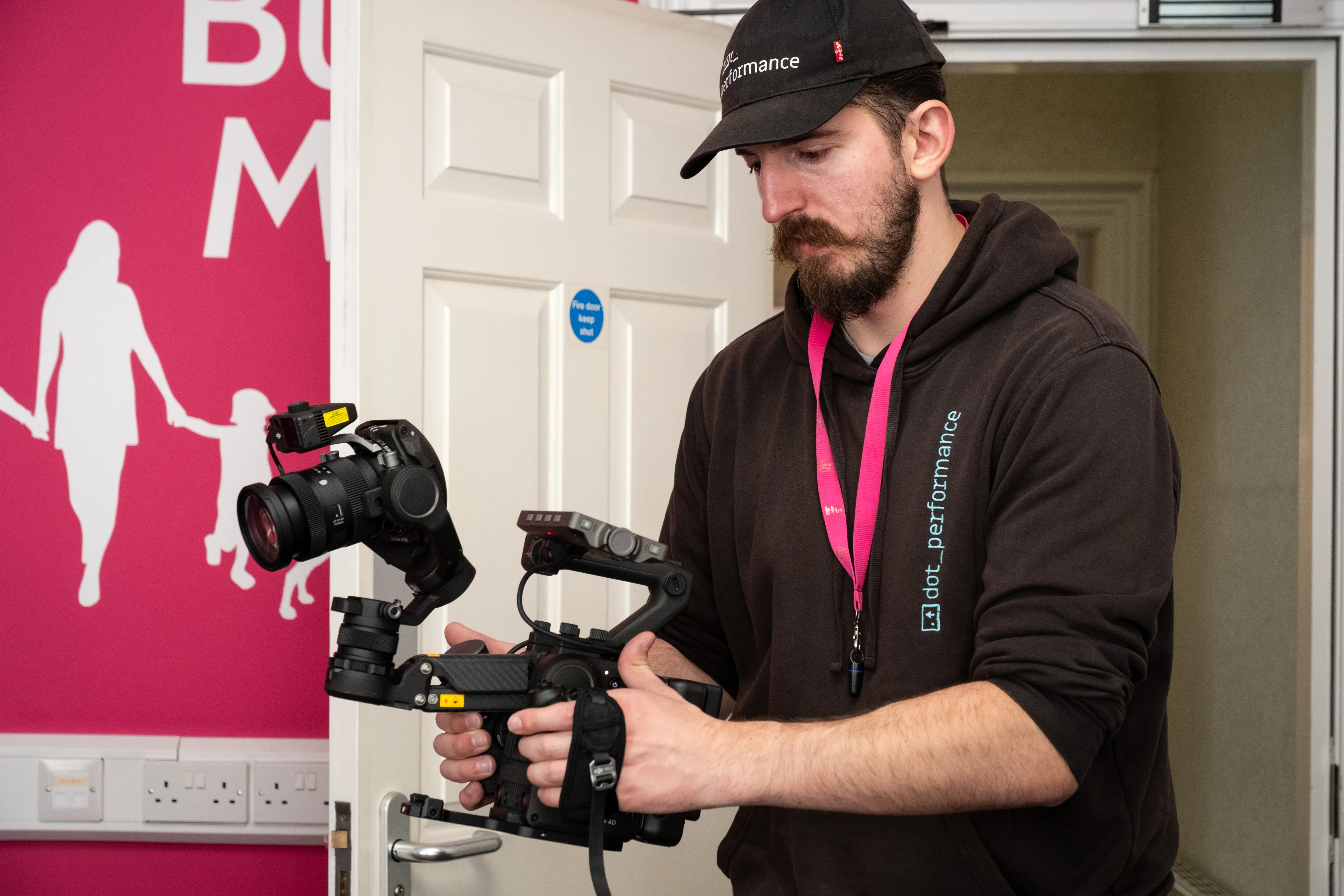 Will Oates operating a DJI Ronin 4D cinema camera on location for DotPerformance, wearing a DotPerformance branded cap and hoodie