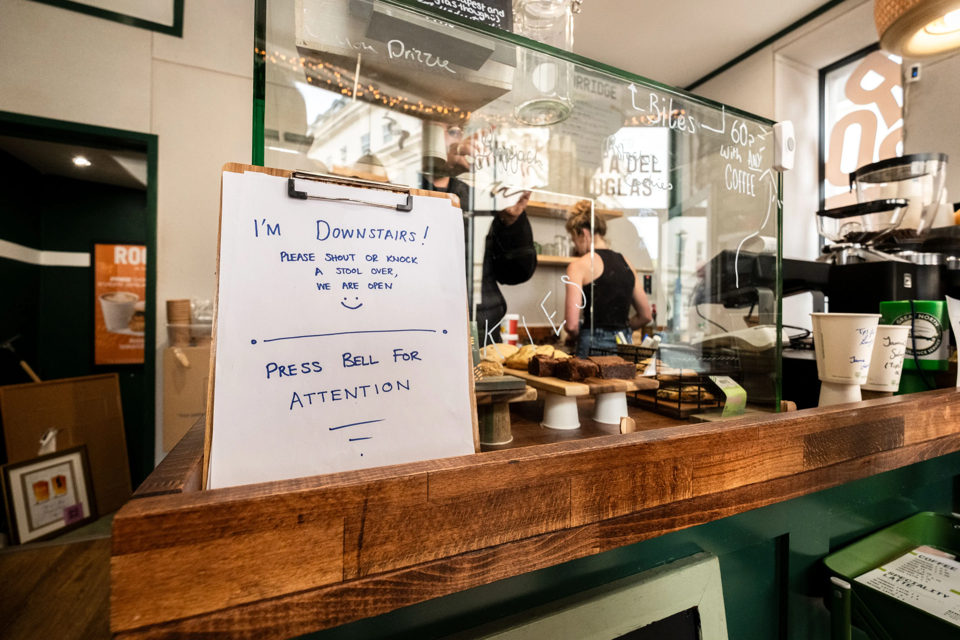 A handwritten sign on a café counter. Pastries and coffee cups on display.