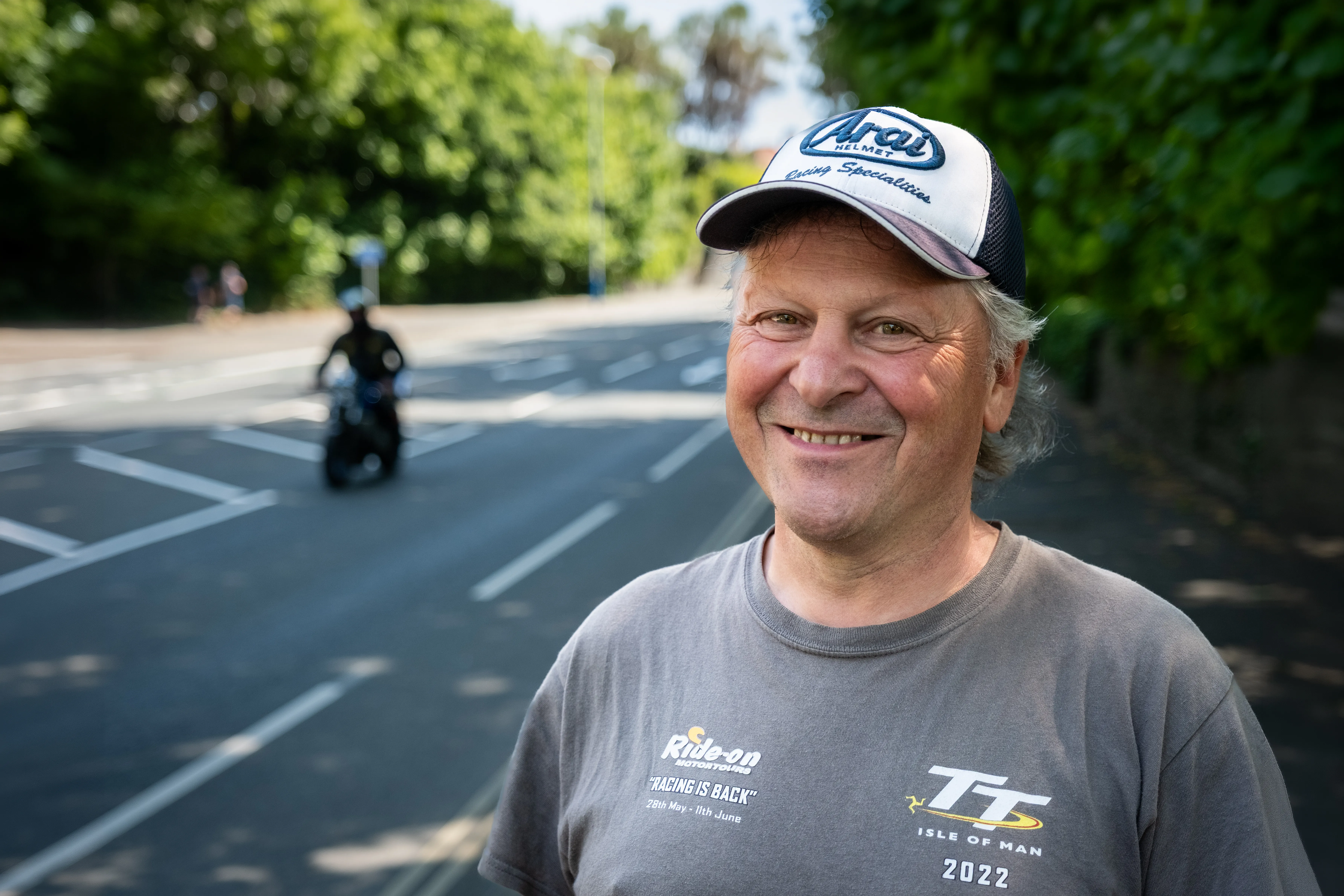 Jan Peters from Netherlands, an Isle of Man TT Marshal, smiling outdoors for Behind the Tabard TT Marshals Series, highlighting marshal stories, in a grey t-shirt and arai cap