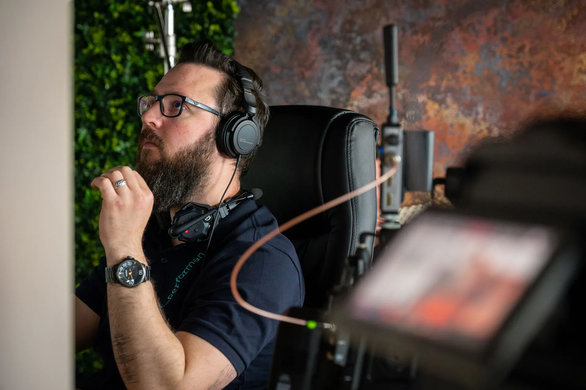 Nico van Loggerenberg wearing headphones and a DotPerformance branded top monitoring a live camera feed during a podcast production at DotPerformance studios on the Isle of Man