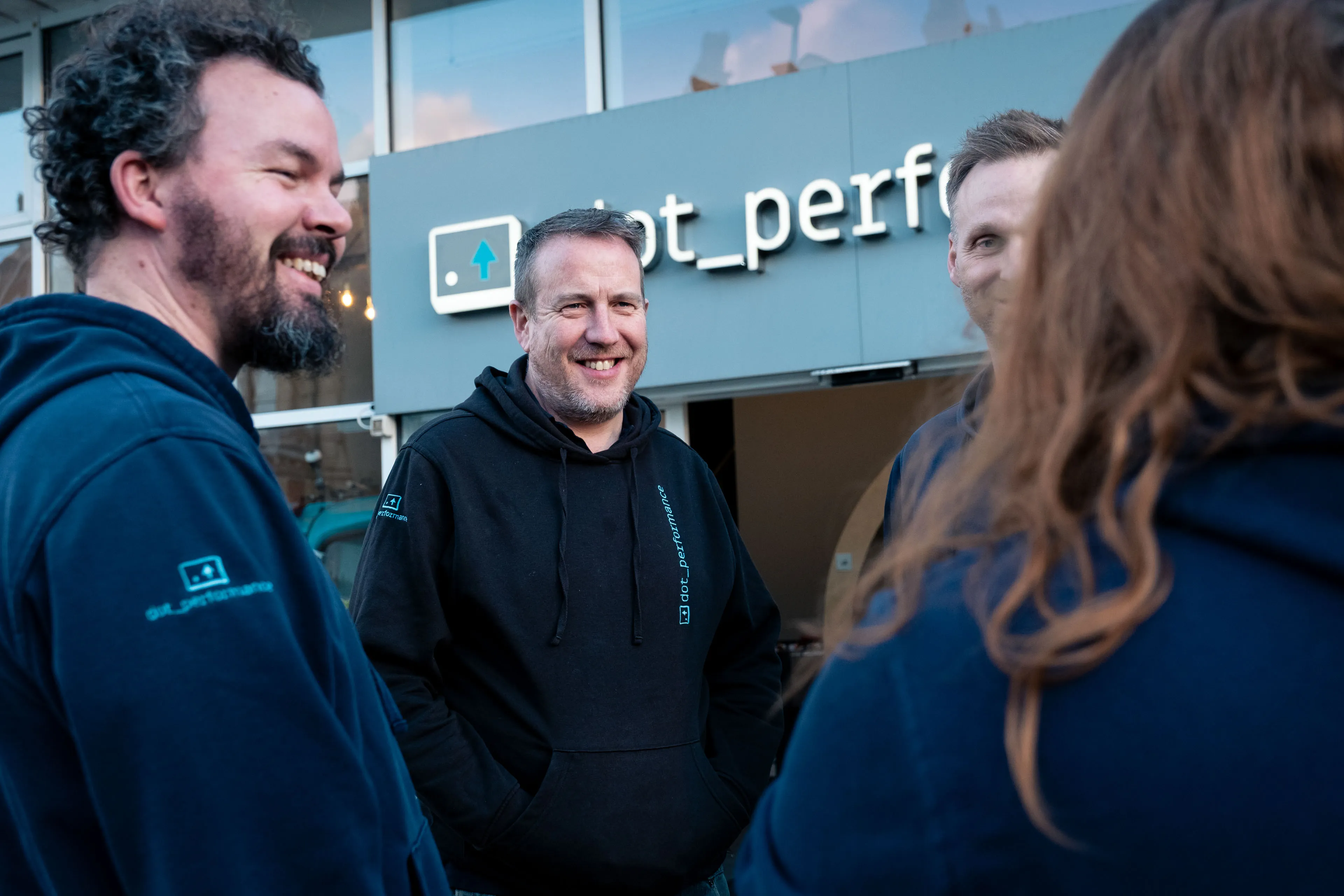Simon King with DotPerformance team members (Adrian Crellin, John Beaty and Paula Hamilton) outside the DotPerformance office in Douglas, Isle of Man, with the agency signage visible behind the group.