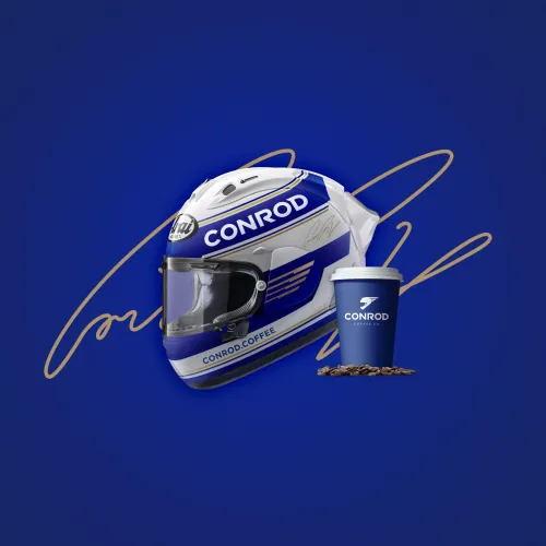 A blue and white racing helmet with "Conrod" branding is shown next to a blue coffee cup and scattered beans, set against a dark blue background.