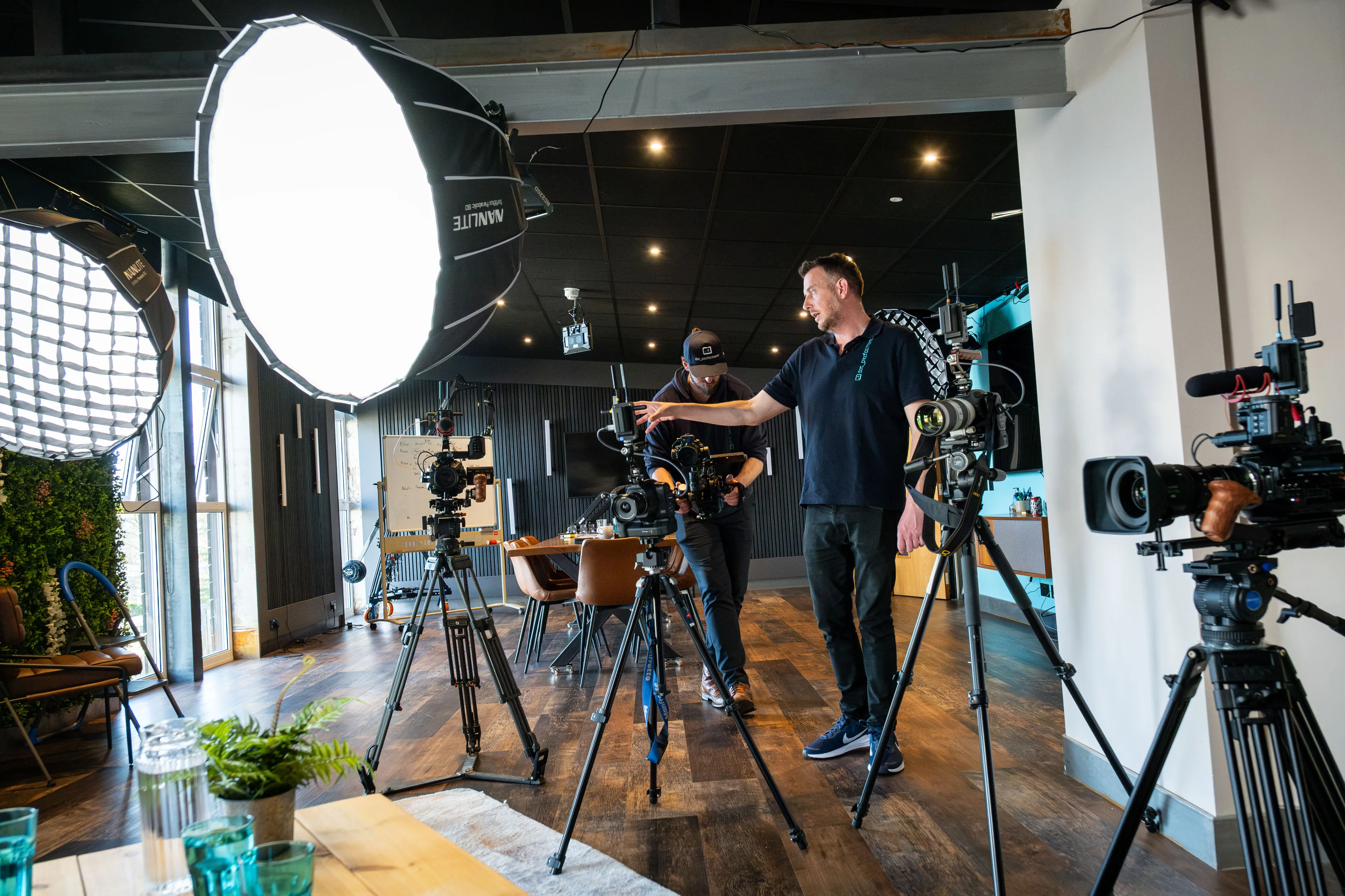 Andy Orton and Will Oates setting up multiple cinema cameras and large softbox lighting in a modern studio space during a podcast or interview production on the Isle of Man