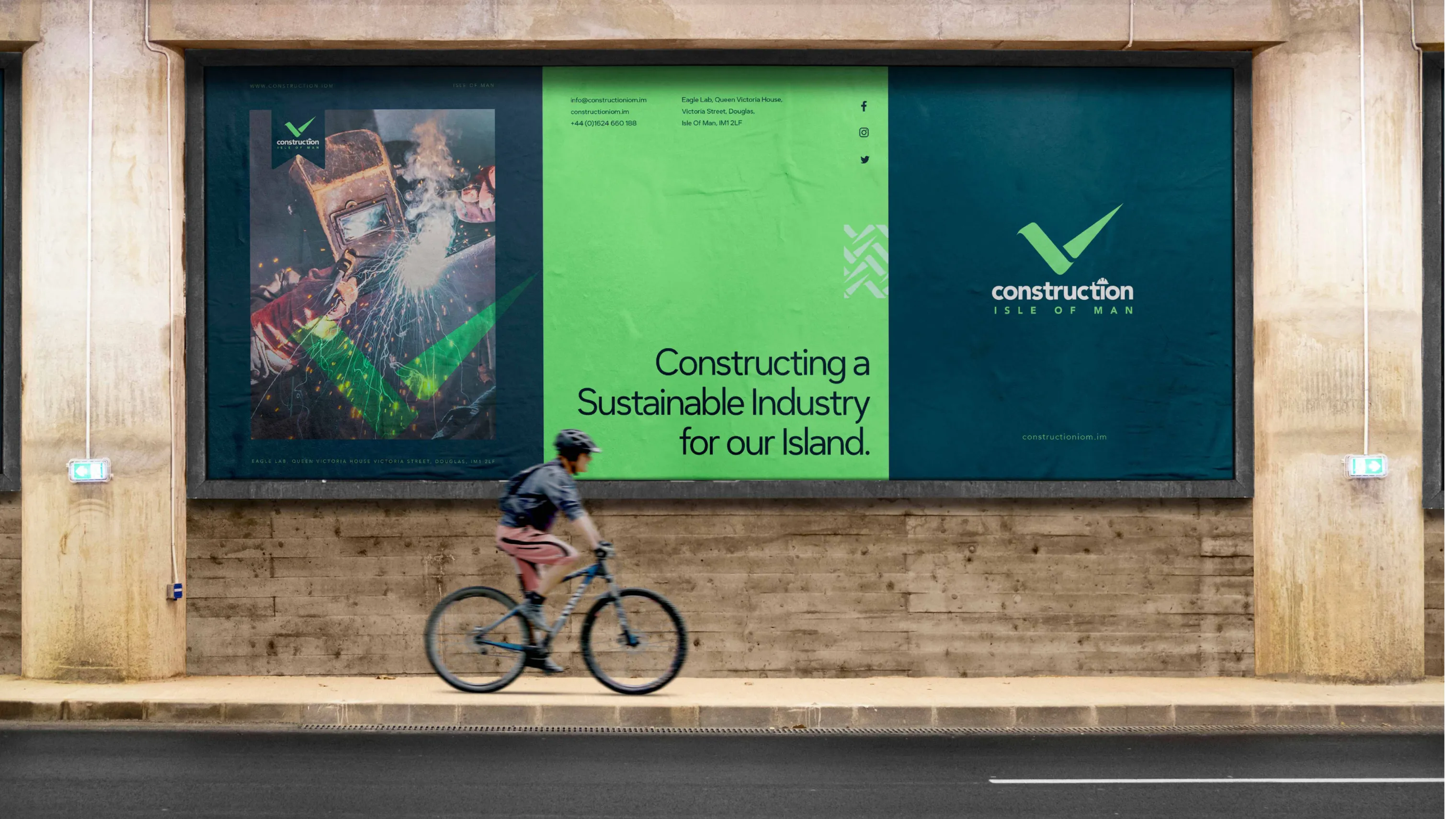 Outdoor billboard on a building exterior displaying Construction Isle of Man logo and the message Constructing a Sustainable Industry for our Island with a cyclist visible in the foreground