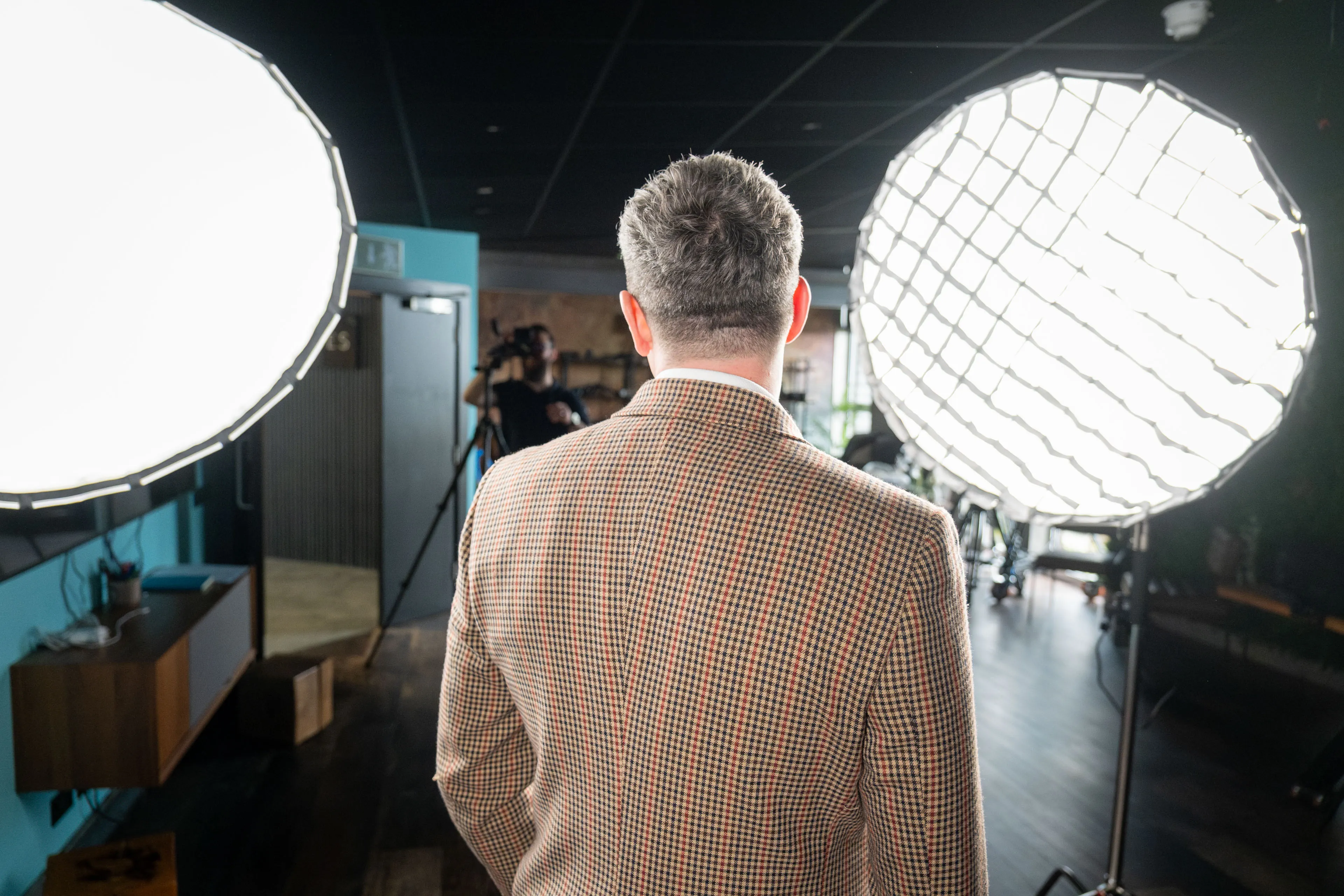 View from behind a headshot subject looking towards two large softbox lights, with a photographer setting up in the background at DotPerformance Studio
