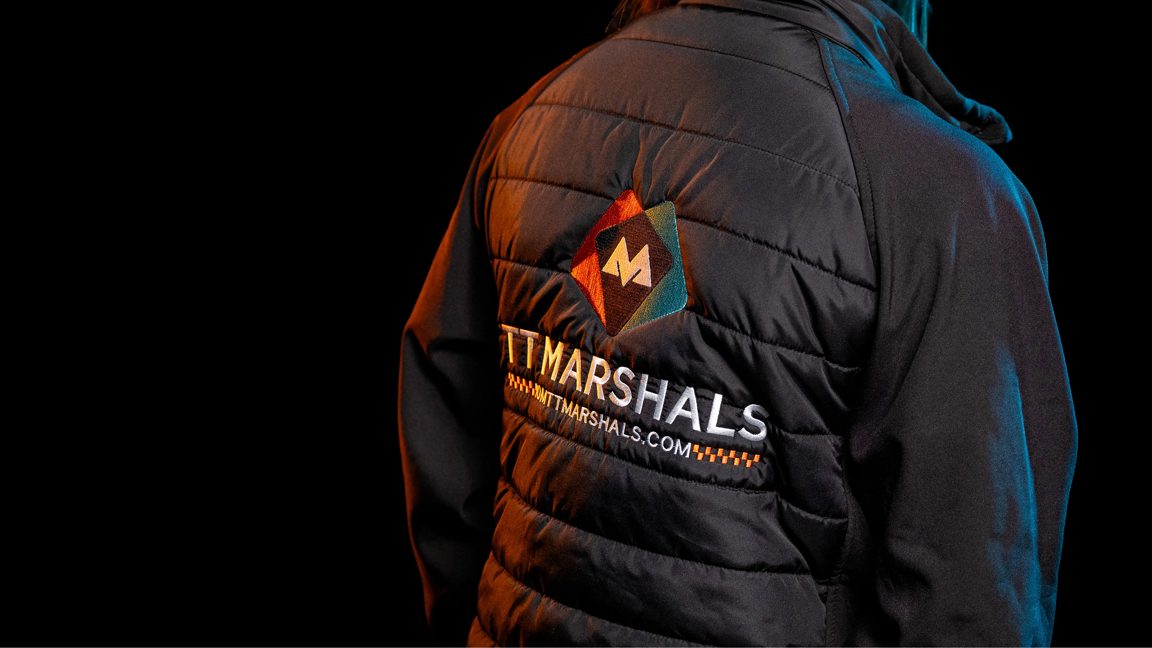 Back of tt marshals softshell jacket merchandise for tt 2026. Set against a black background with orange accent lighting.