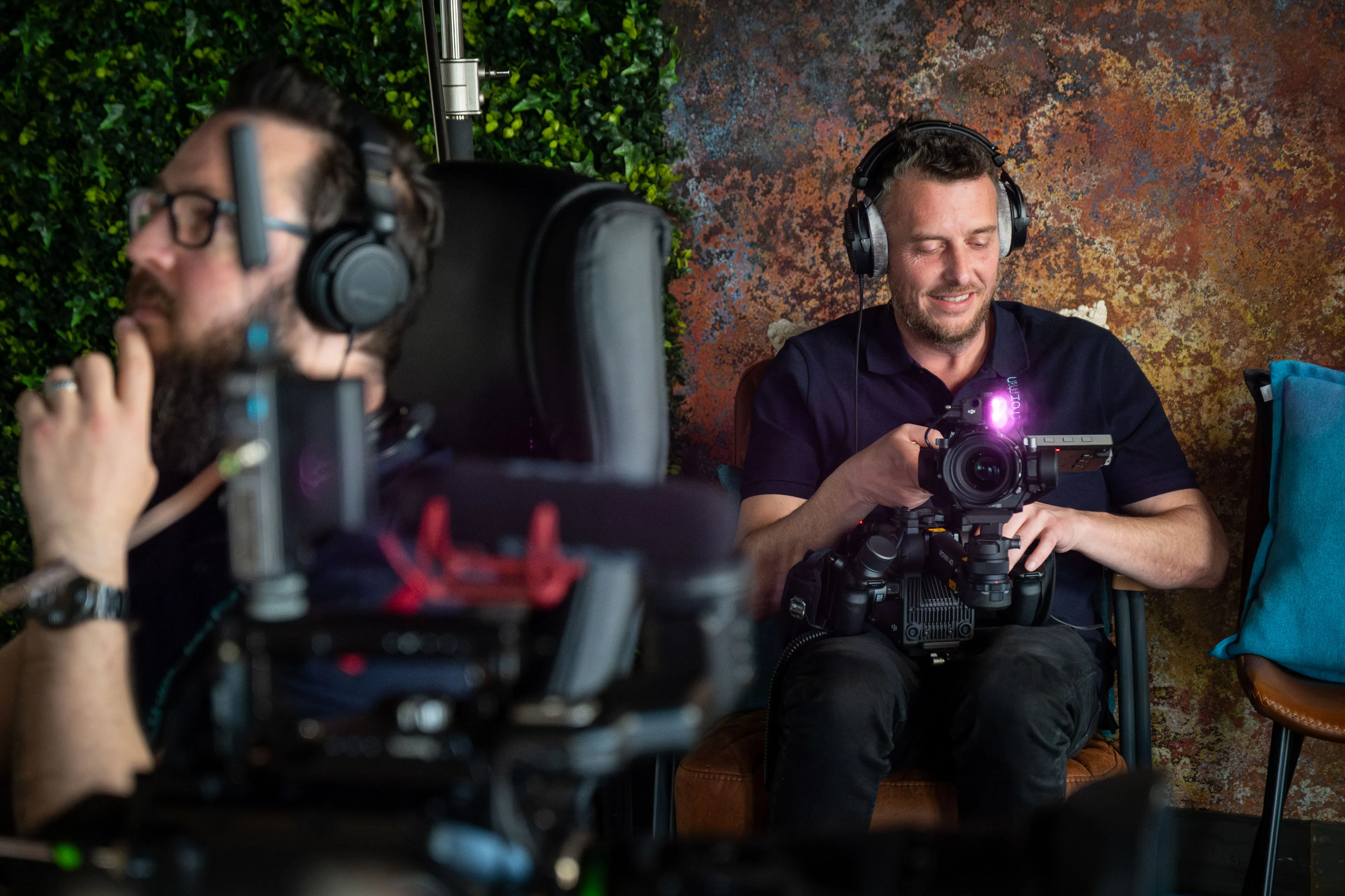 Nico van Loggerenberg and Andy Orton wearing headphones during a podcast studio production on the Isle of Man, one monitoring audio and one operating a DJI Ronin 4D camera