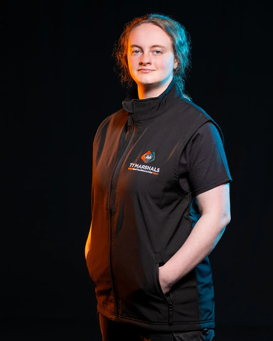 Chloe Hampson wearing the official TT Marshals 2026 black polo shirt, featuring the TT Marshals logo. Exclusive marshal merchandise for the Isle of Man TT 2026.