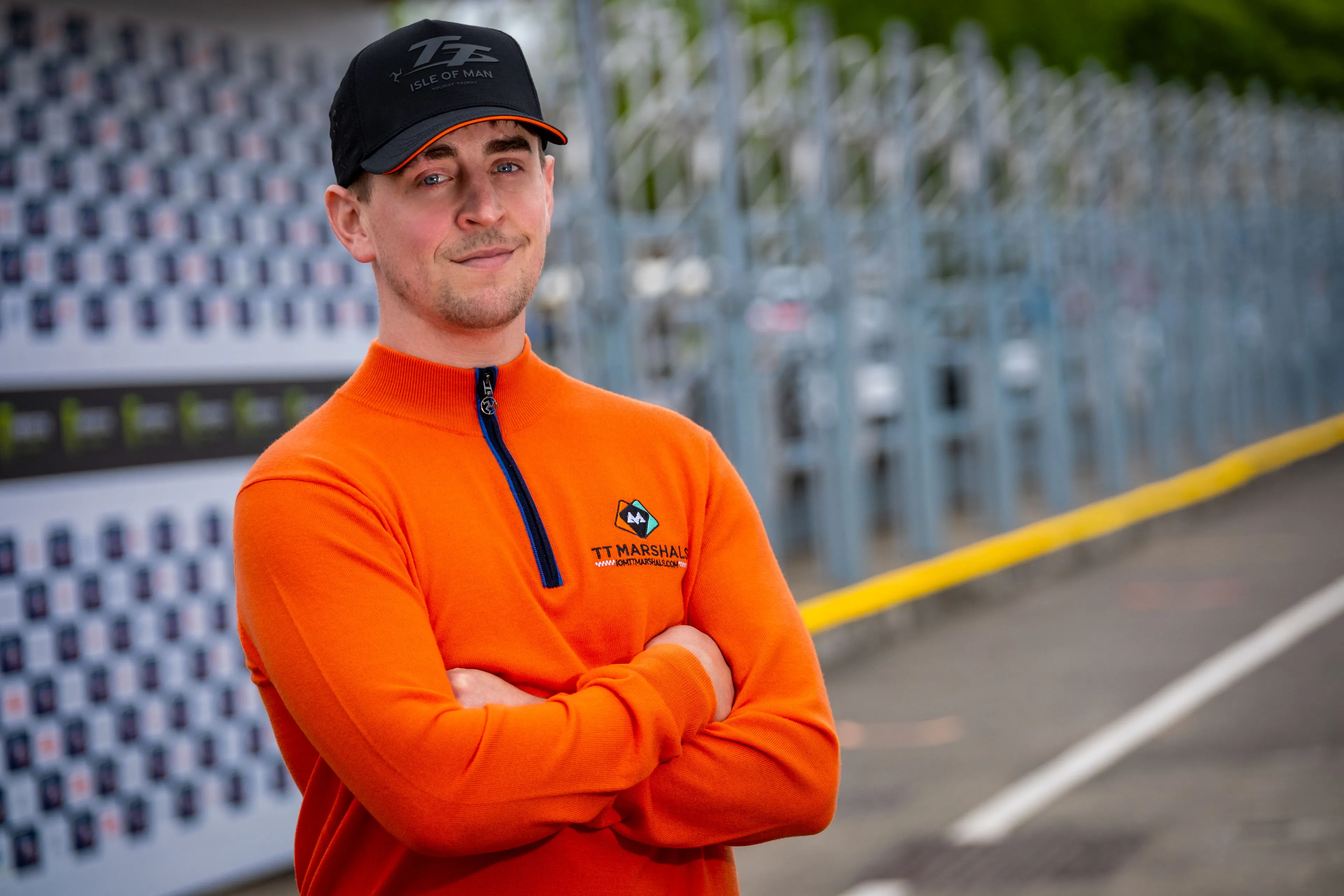 Dom Herbertson standing in front of the podium by the TT Grandstand wearing the TT Marshals Albion Knitware prize jumper