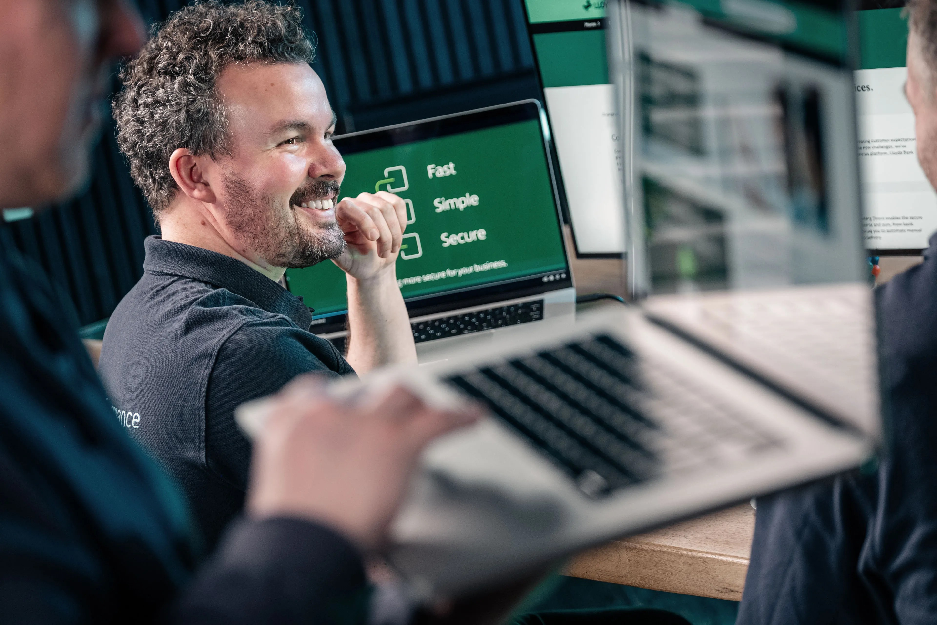 Adrian Crellin reviewing UI design work on a laptop with a colleague at the DotPerformance office in Douglas, Isle of Man, with client website designs visible on screen