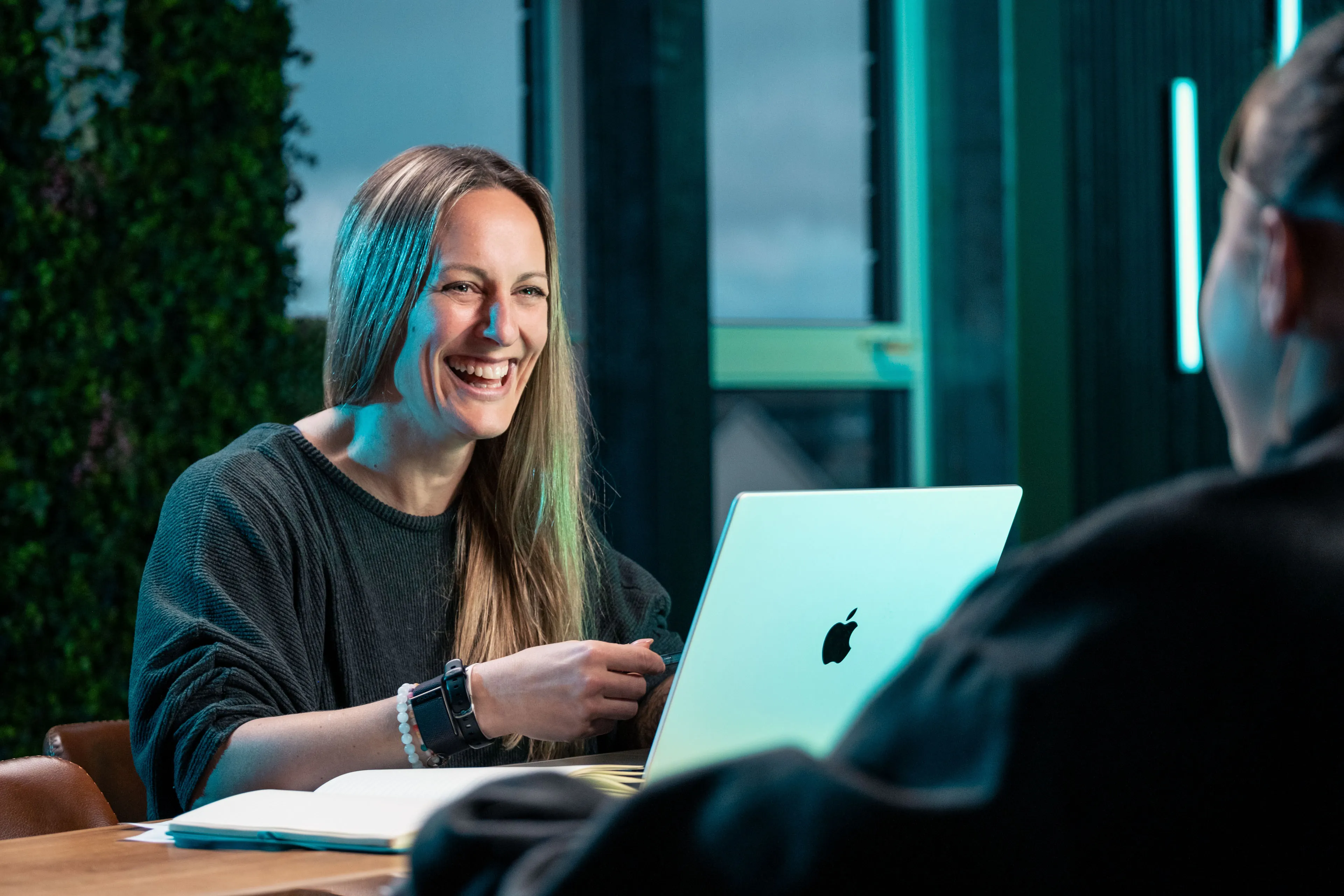 Rachel Fabrizio laughing during a client meeting at the DotPerformance office in Douglas, Isle of Man, with an Apple MacBook open on the table