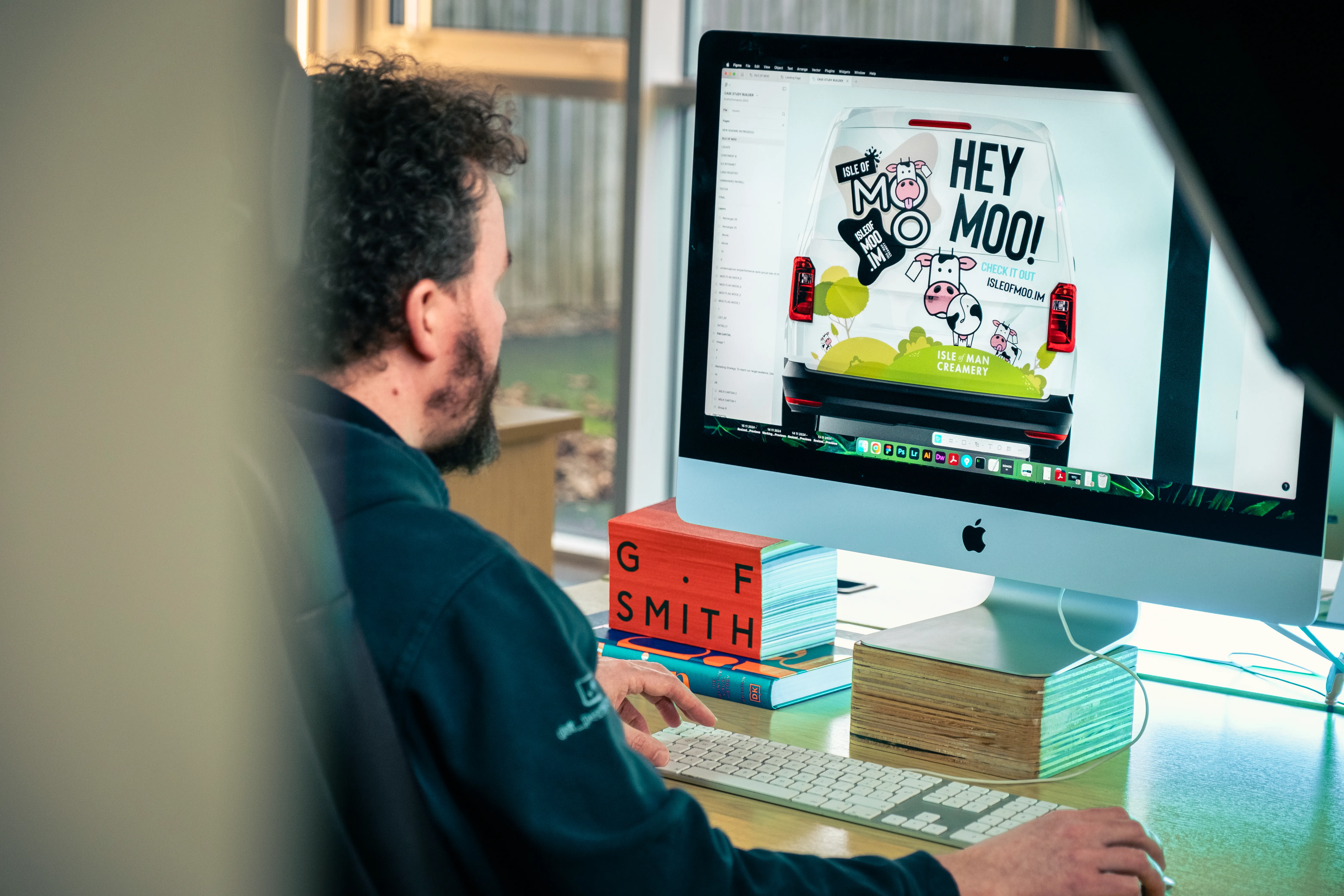 Adrian Crellin working on the Isle of Moo vehicle livery design at the DotPerformance studio on the Isle of Man, with the van rear design displayed on an iMac