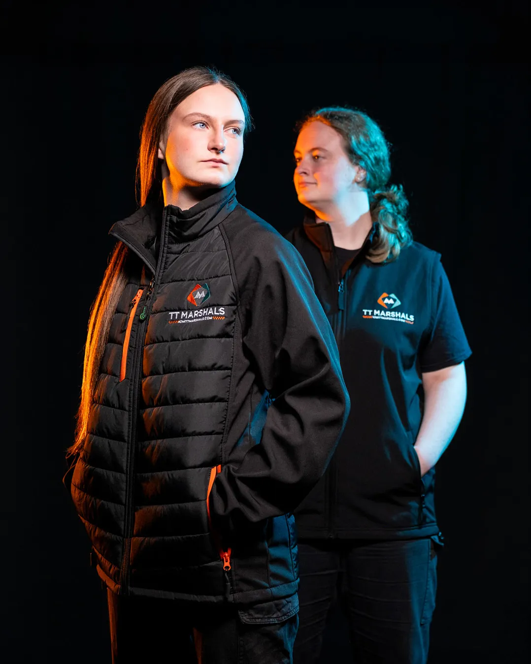 Caitlin and Chloe Hampson wearing the official TT Marshals 2026 black gilet and softshell padded jacket, featuring the TT Marshals logo. Exclusive marshal merchandise for the Isle of Man TT 2026.