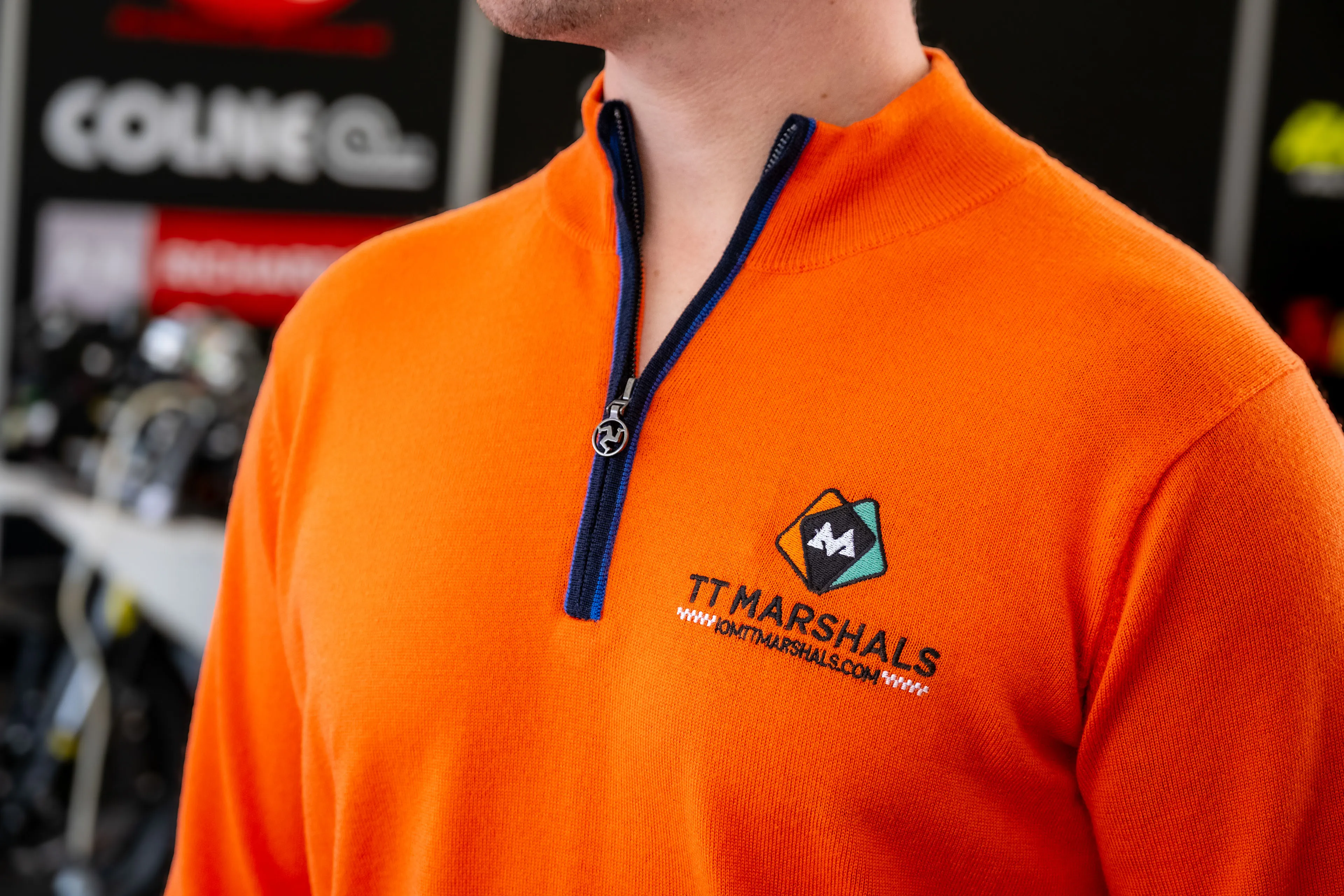 Close-up of the TT Marshals Albion Knitware prize jumper worn by Dom Herbertson, showing the embroidered logo and Manx triskelion zip pull