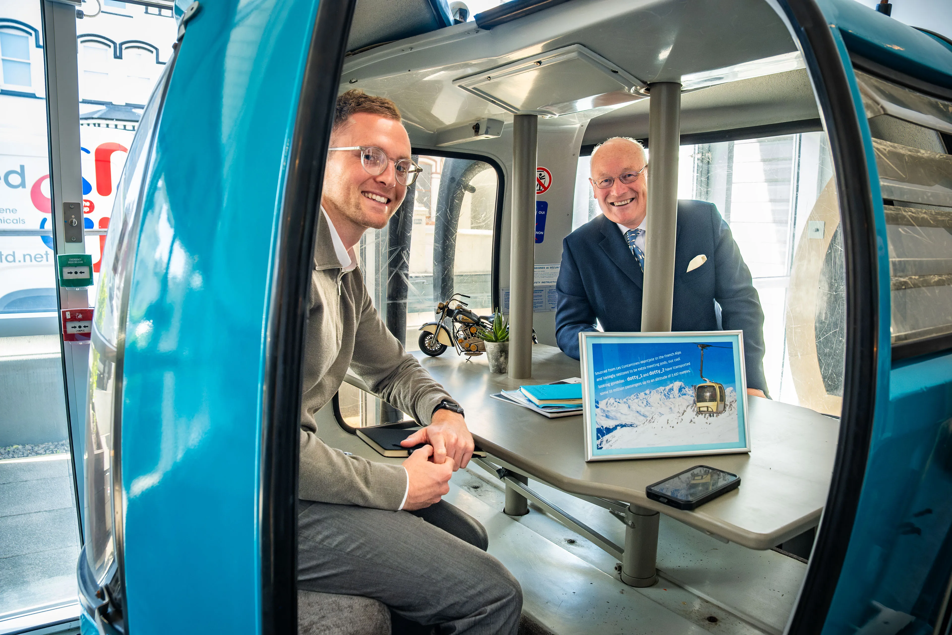 Lieutenant General Sir John Lorimer KCB DSO MBE and his assistant smiling for a photo inside DotPerformance's converted gondola meeting pod