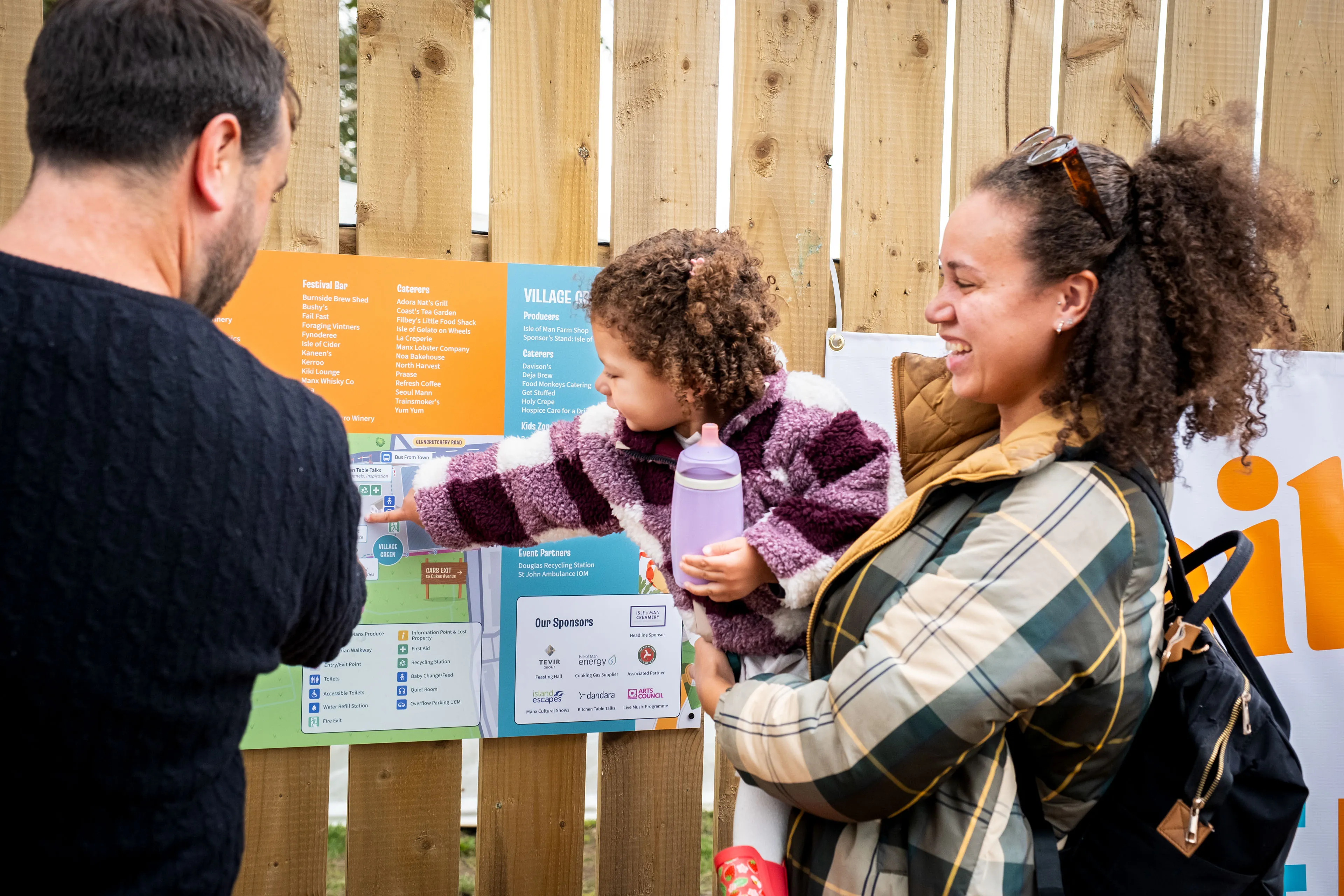 A family with a young child pointing at the Village Green section of the Big Manx Feast site map