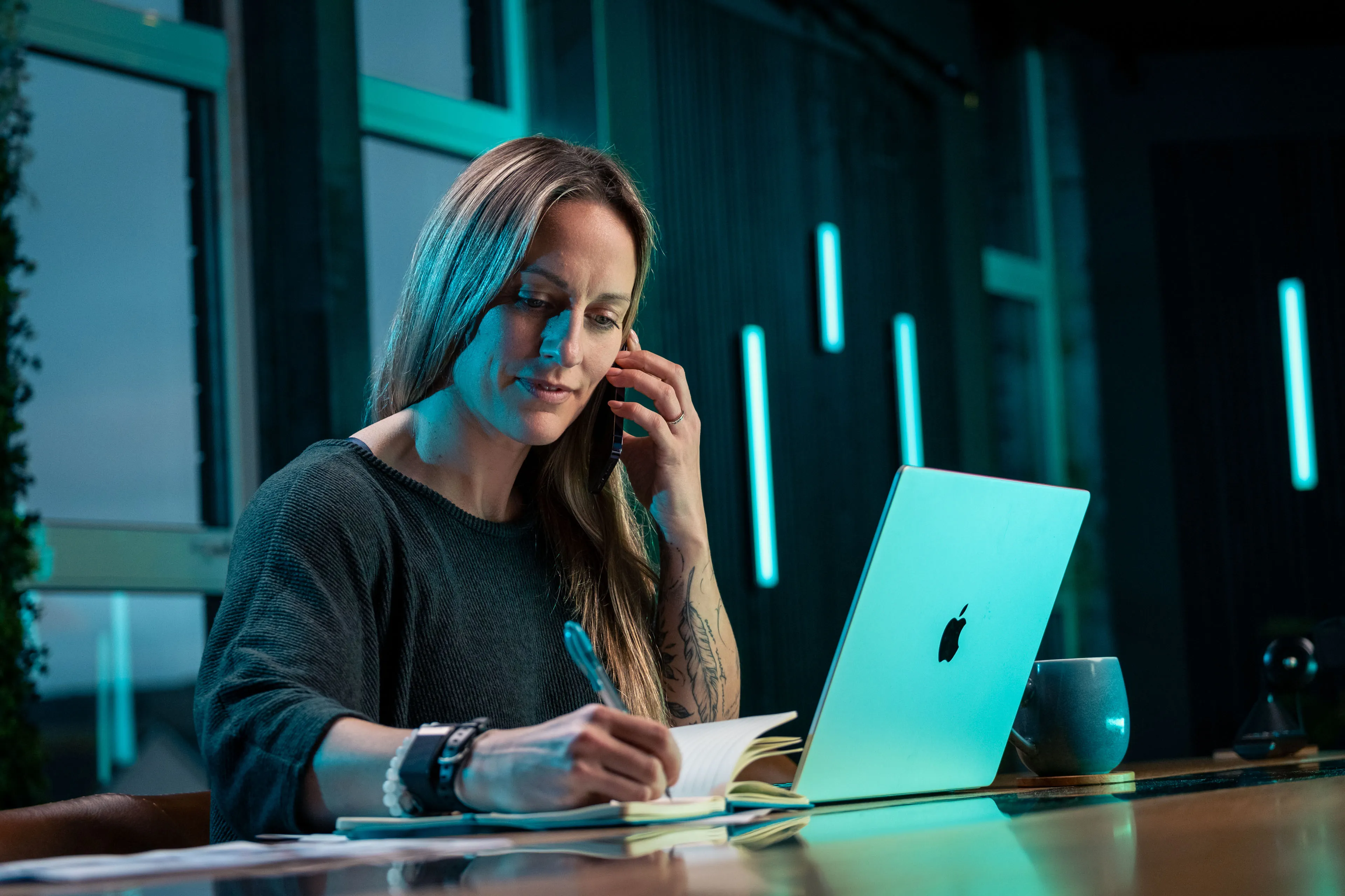 Rachel Fabrizio taking a client call and making notes at her desk at DotPerformance studios on the Isle of Man, with an Apple MacBook open in front of her