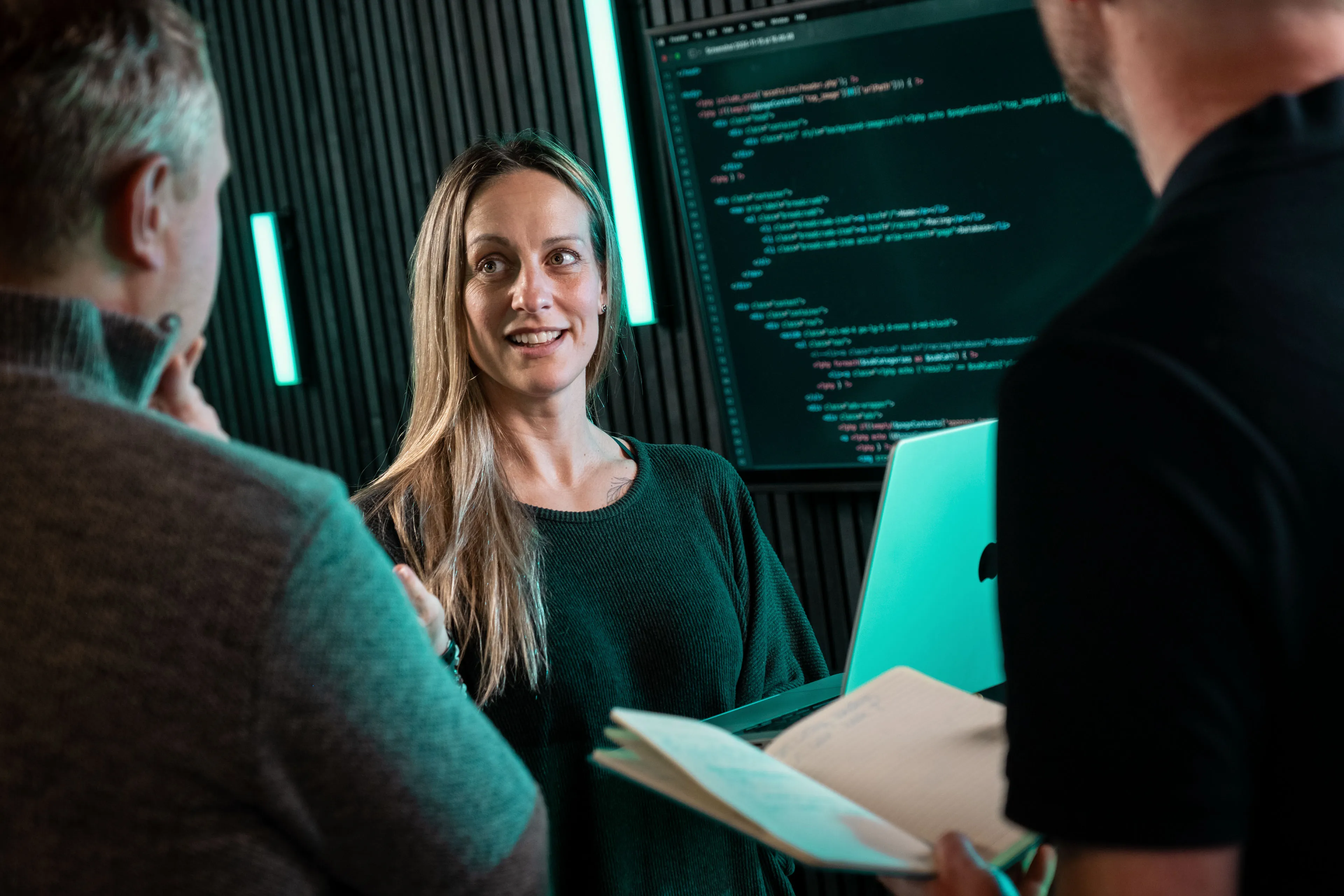 Rachel Fabrizio discussing a development project with DotPerformance colleagues at the agency office in Douglas, Isle of Man, with front-end code displayed on a large monitor behind the group