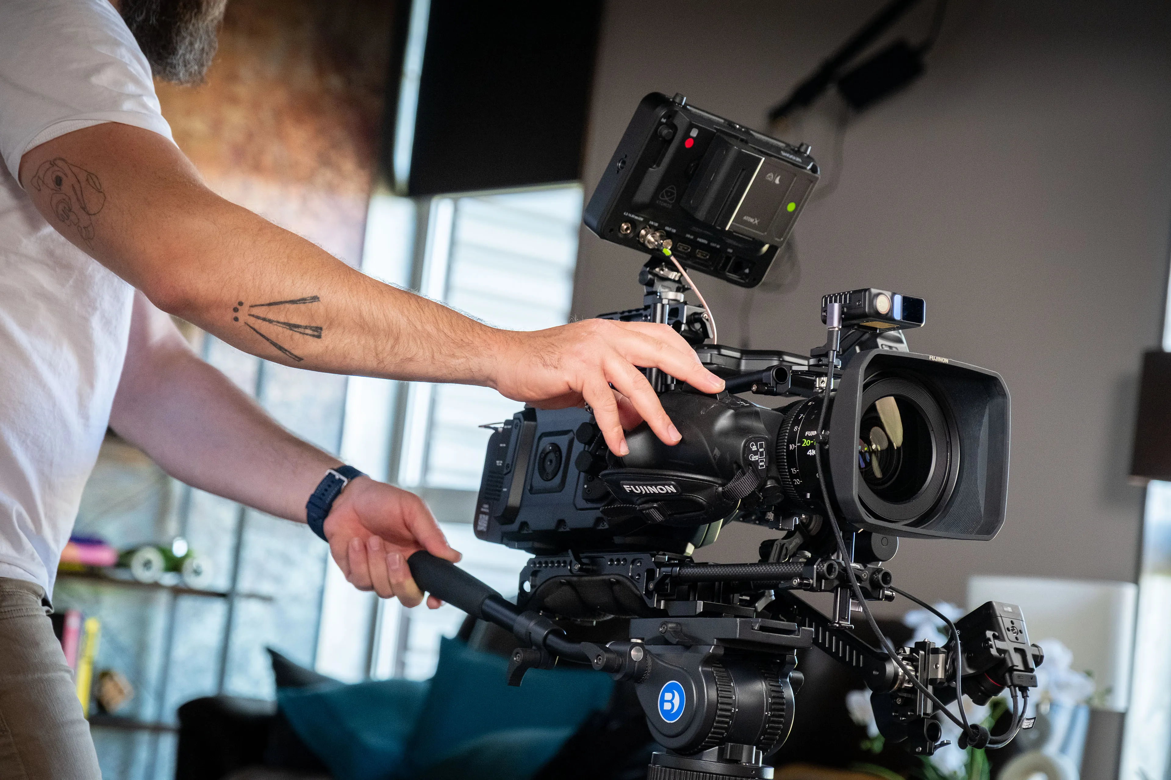 Close-up of Nico van Loggerenberg's hand adjusting the Fujinon 20-120mm lens on the Blackmagic Ursa Mini camera, with the Atomos Shogun Ultra monitor mounted on top