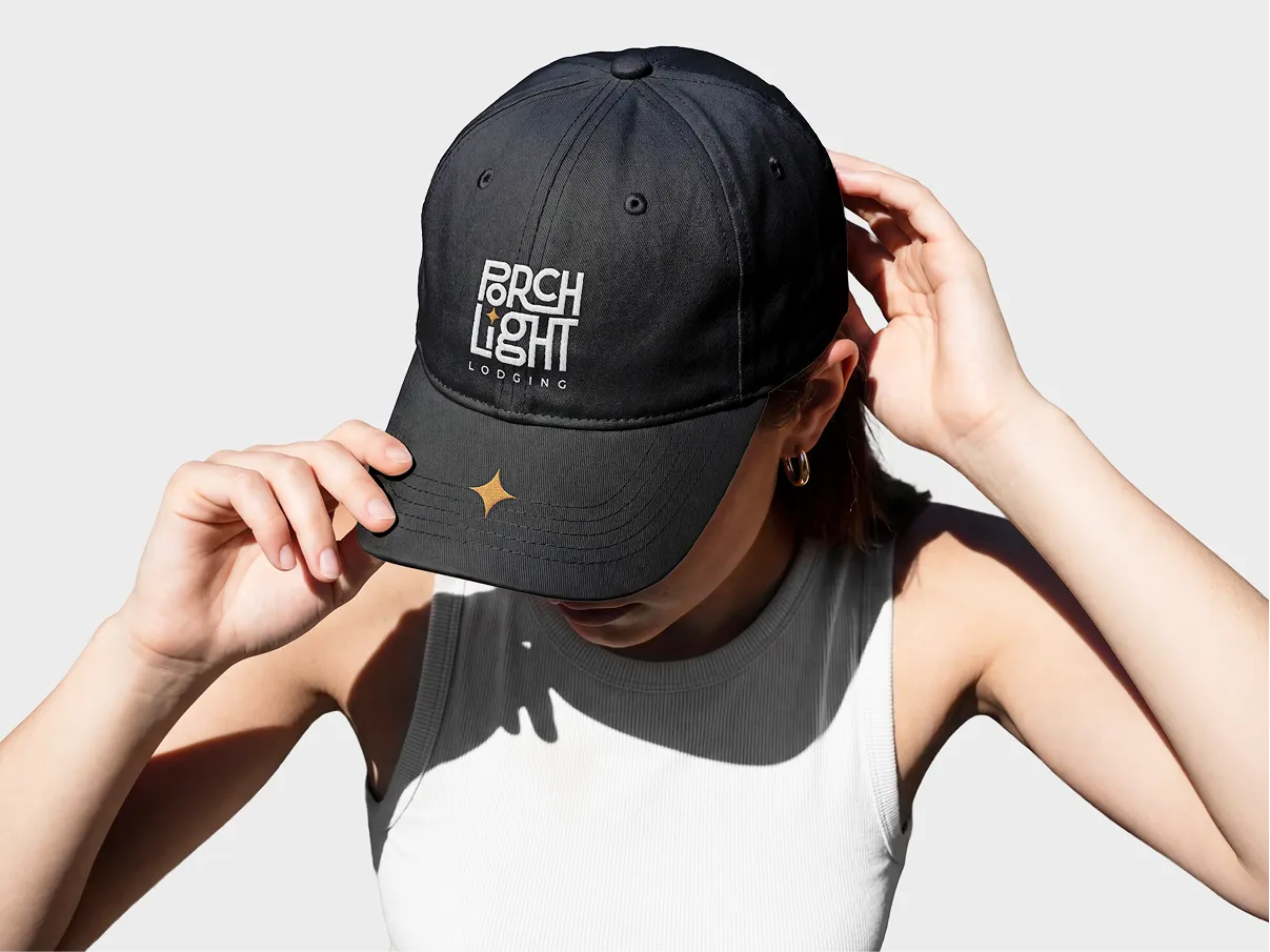 Woman adjusting a black cap embroidered with the white PorchLight Lodging logo and a gold star on the peak