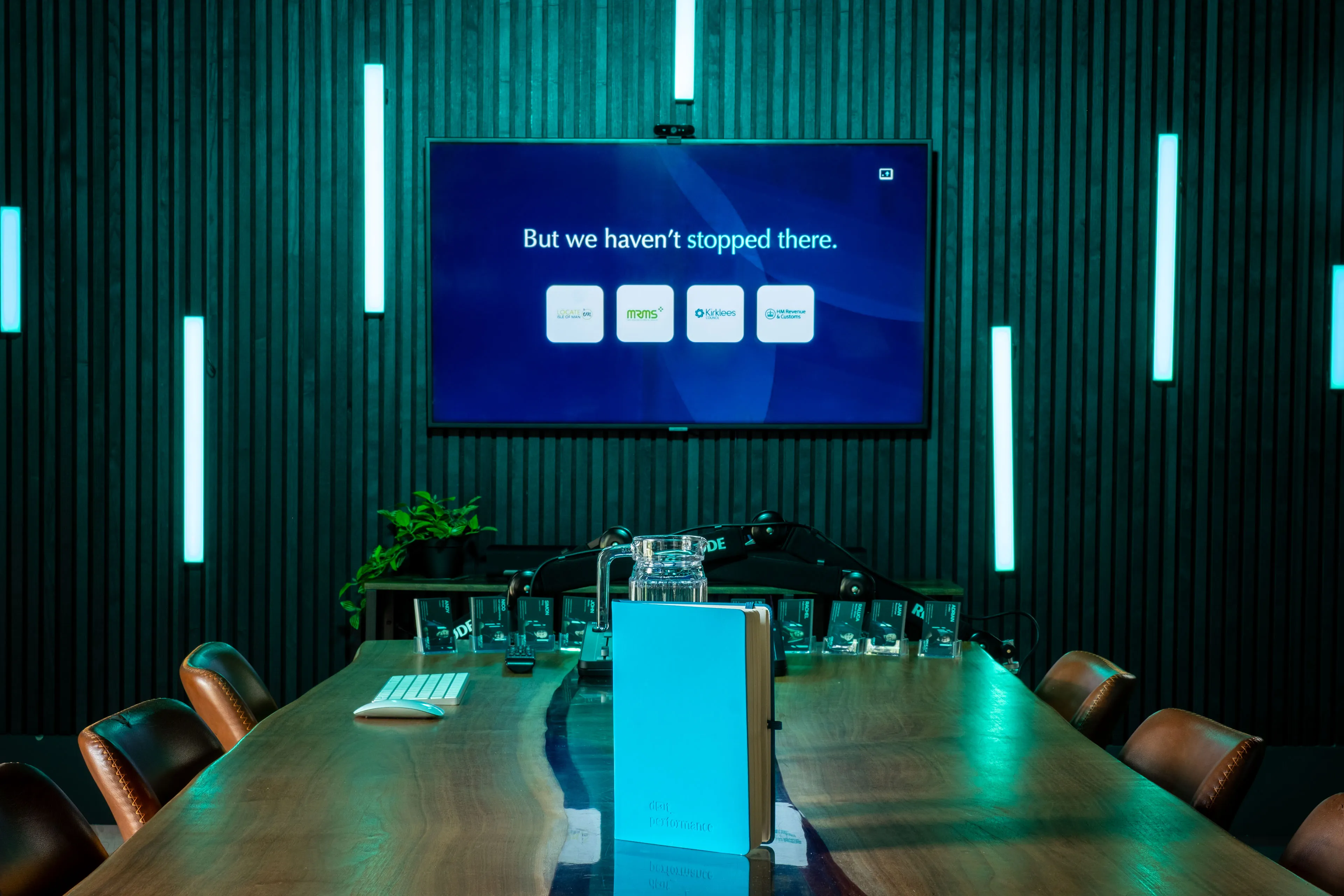 DotPerformance boardroom screen showing the "But we haven't stopped there" slide, listing Locate Isle of Man, MRMS, Kirklees and HMRC from the Innovation Challenge presentation