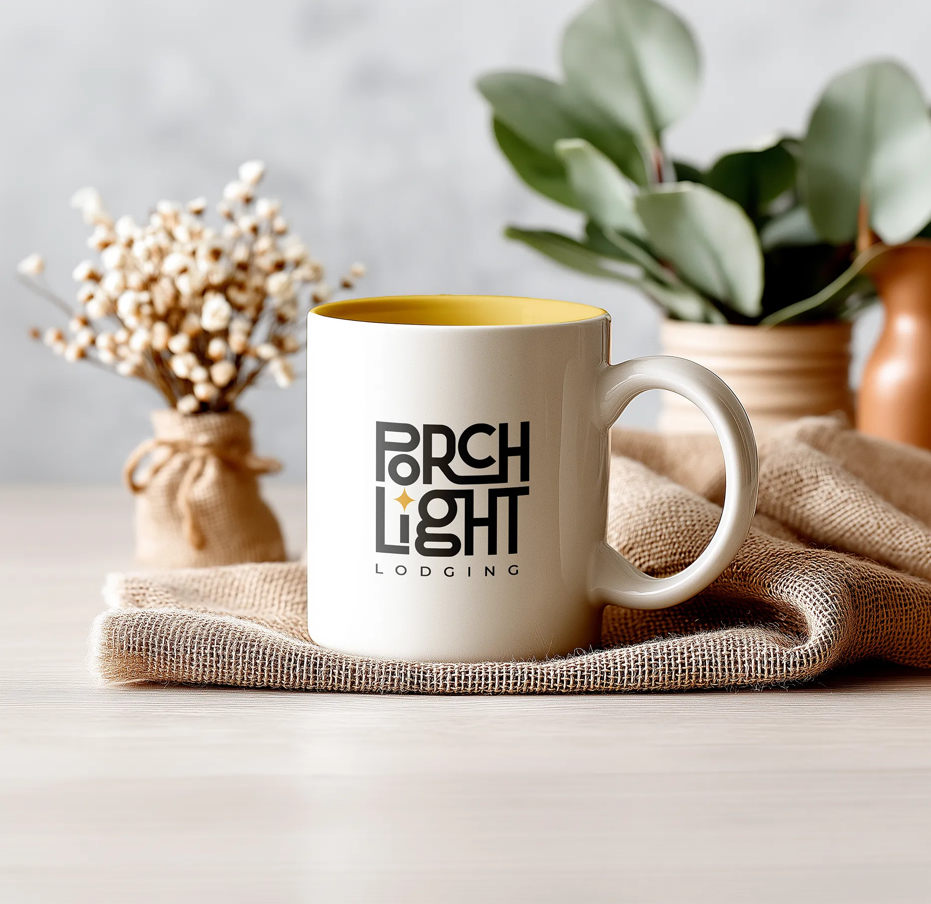 White PorchLight Lodging mug with a gold interior on a hessian cloth beside dried flowers and a potted plant