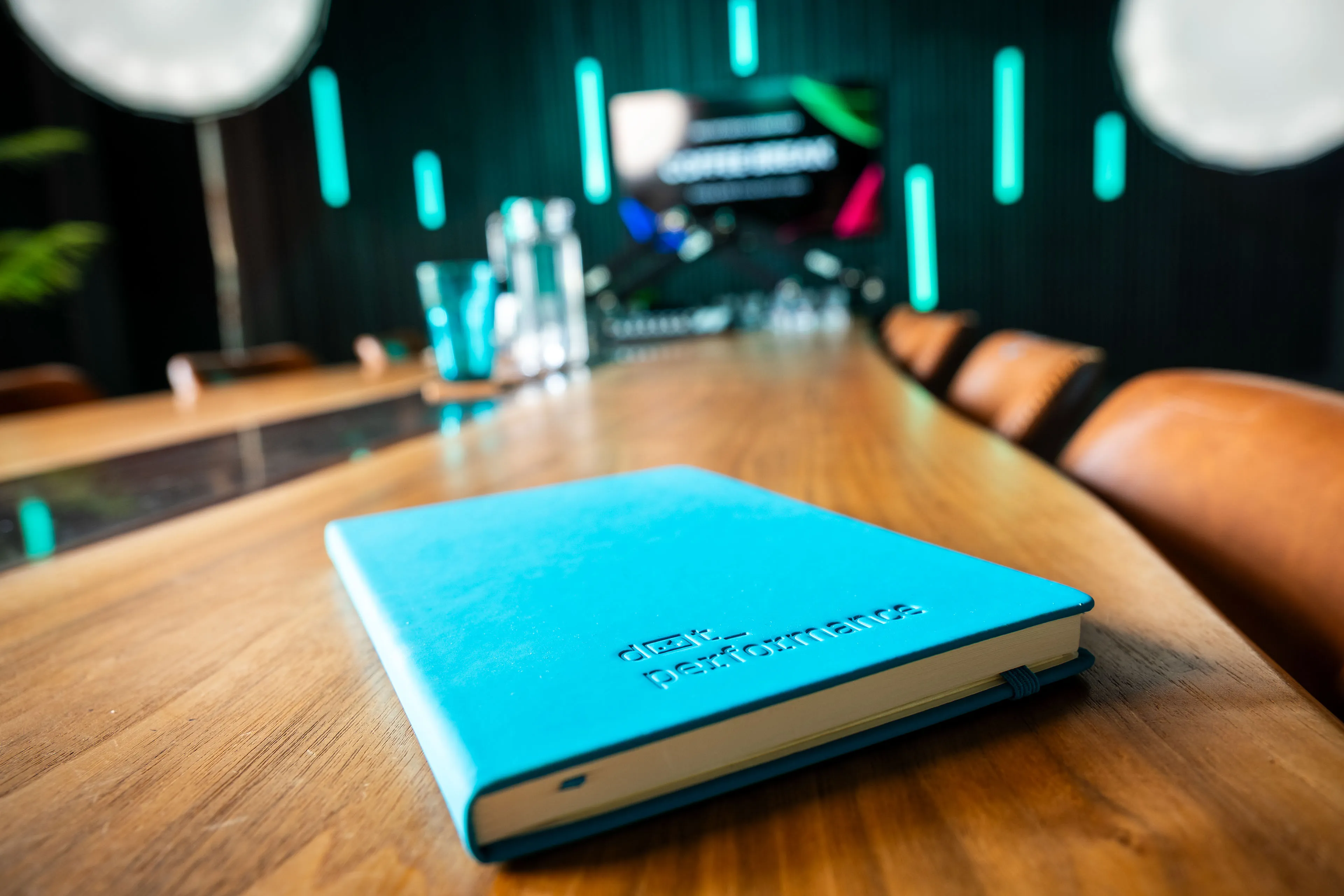Close-up of a teal DotPerformance branded notebook on the boardroom table, with the Innovation Challenge 2026 livestream visible on screen behind