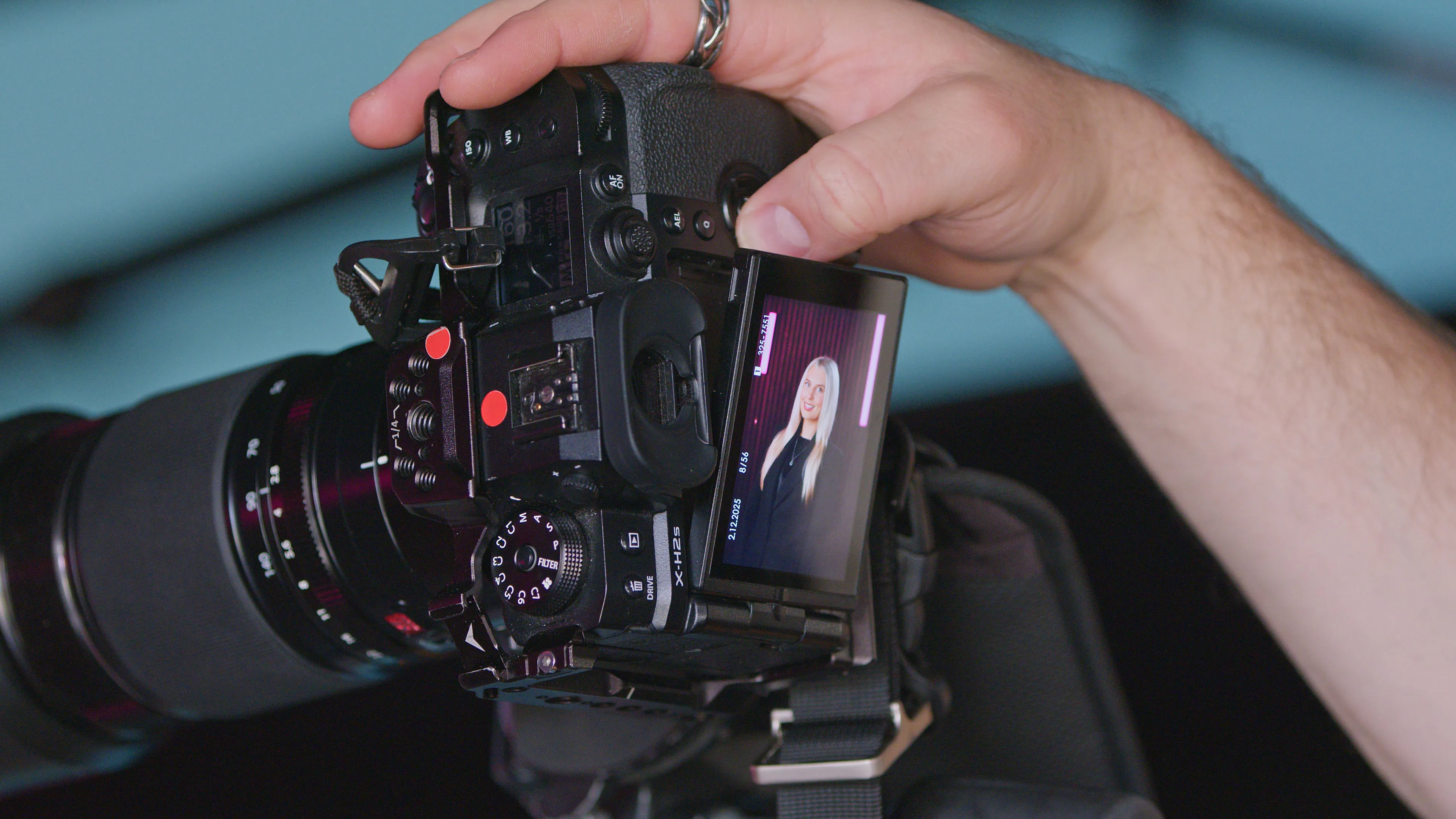 Close-up of hands holding a camera with a portrait displayed on the screen. The subject is a woman with long blonde hair, set against a dark background.