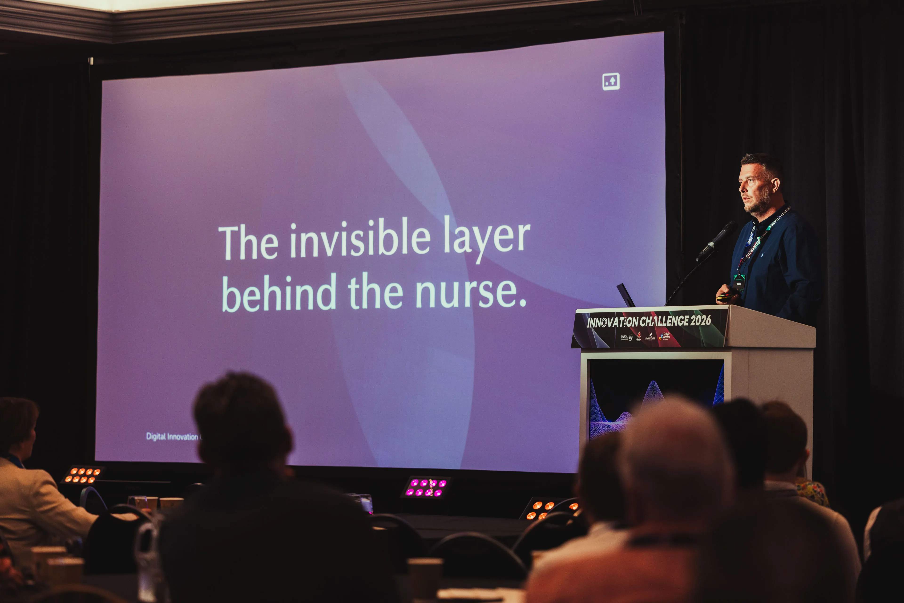 Andy Orton speaking at the podium in front of a screen reading "The invisible layer behind the nurse" during DotPerformance's presentation