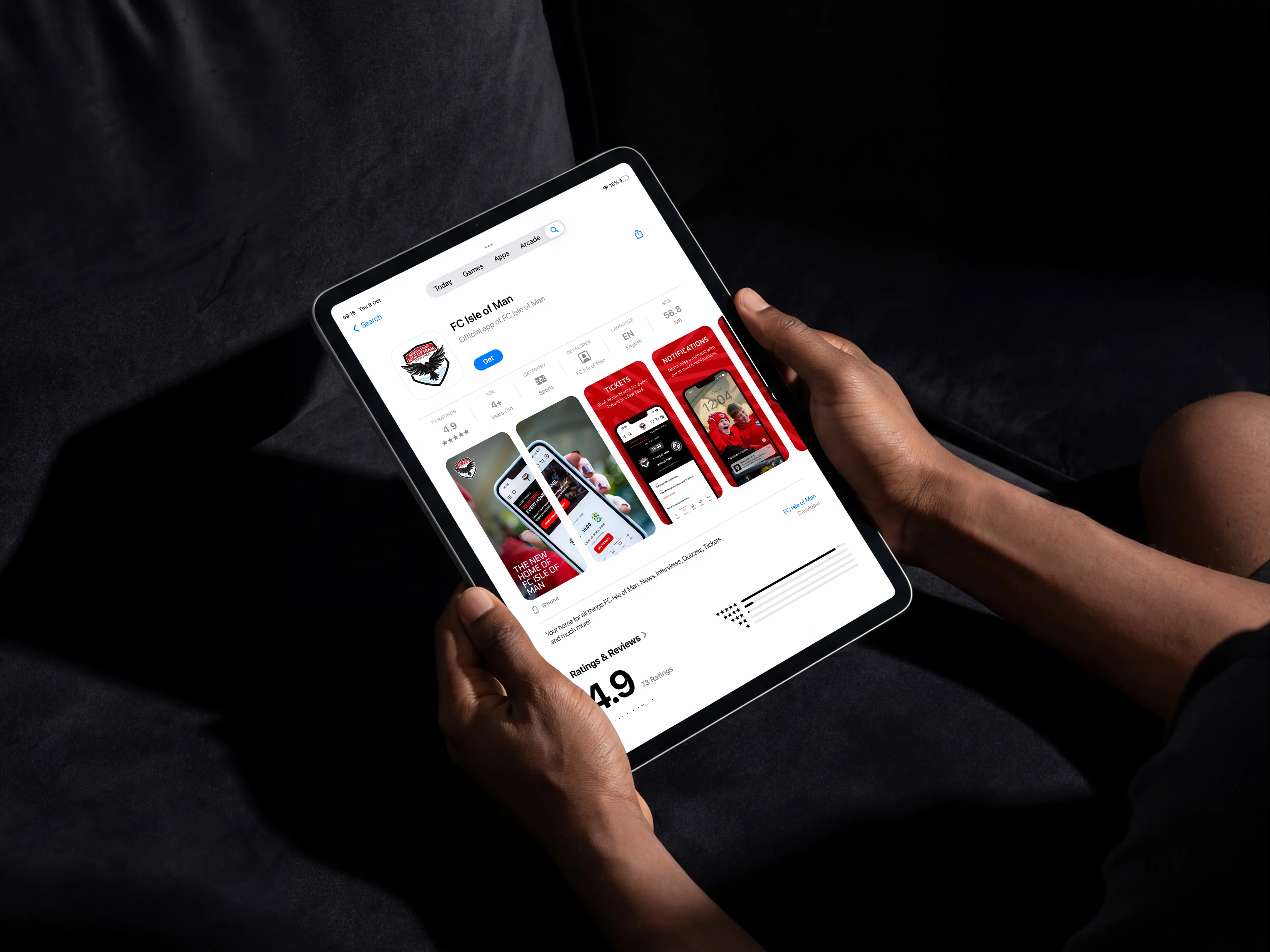 Person on a dark sofa holding an iPad showing the FC Isle of Man app's App Store listing, with feature screenshots and a 4.9 rating