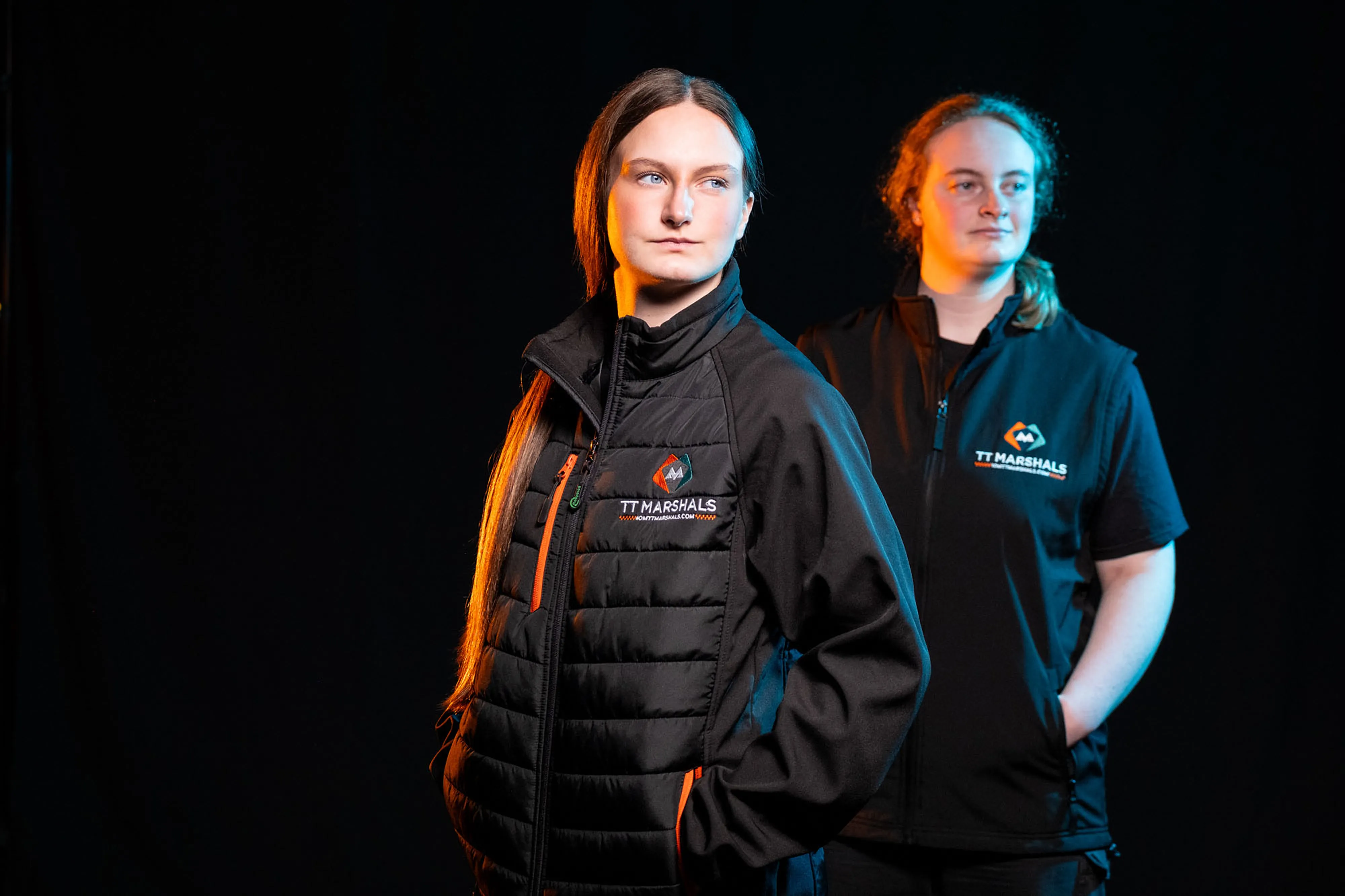 Caitlin Hampson and Chloe Hampson wearing the official TT Marshals 2026 black gilet and softshell padded jacket, featuring the TT Marshals logo. Exclusive marshal merchandise for the Isle of Man TT 2026.
