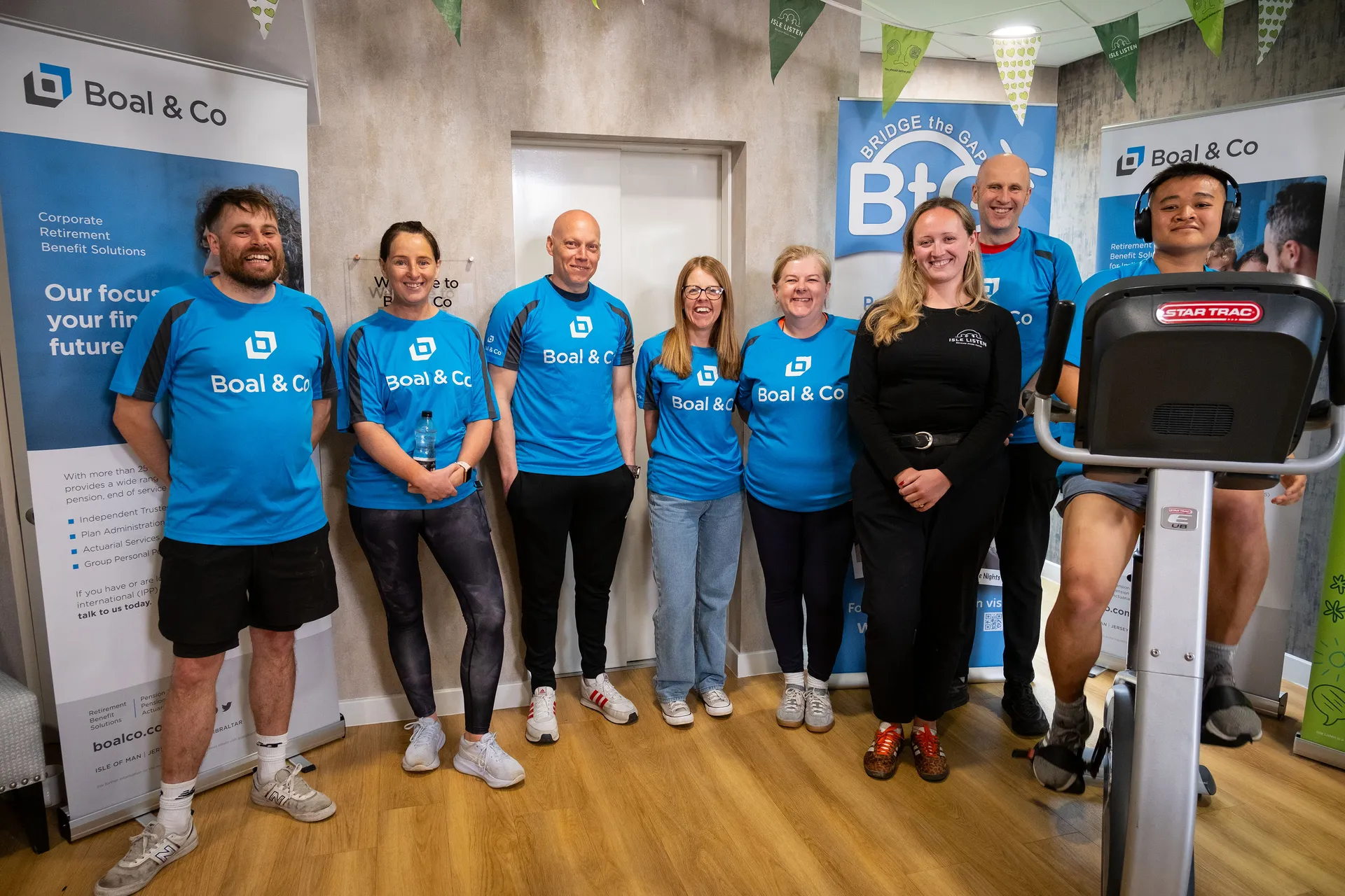 Andrew Cover, Karen McHale, Greg Collins, Vicky Mackie, Christine Evans, James Bassett and Joshua Zote in branded cycling jerseys with Jess Knight from Isle Listen, taken at the Boal & Co office on the Isle of Man during the charity cycling challenge