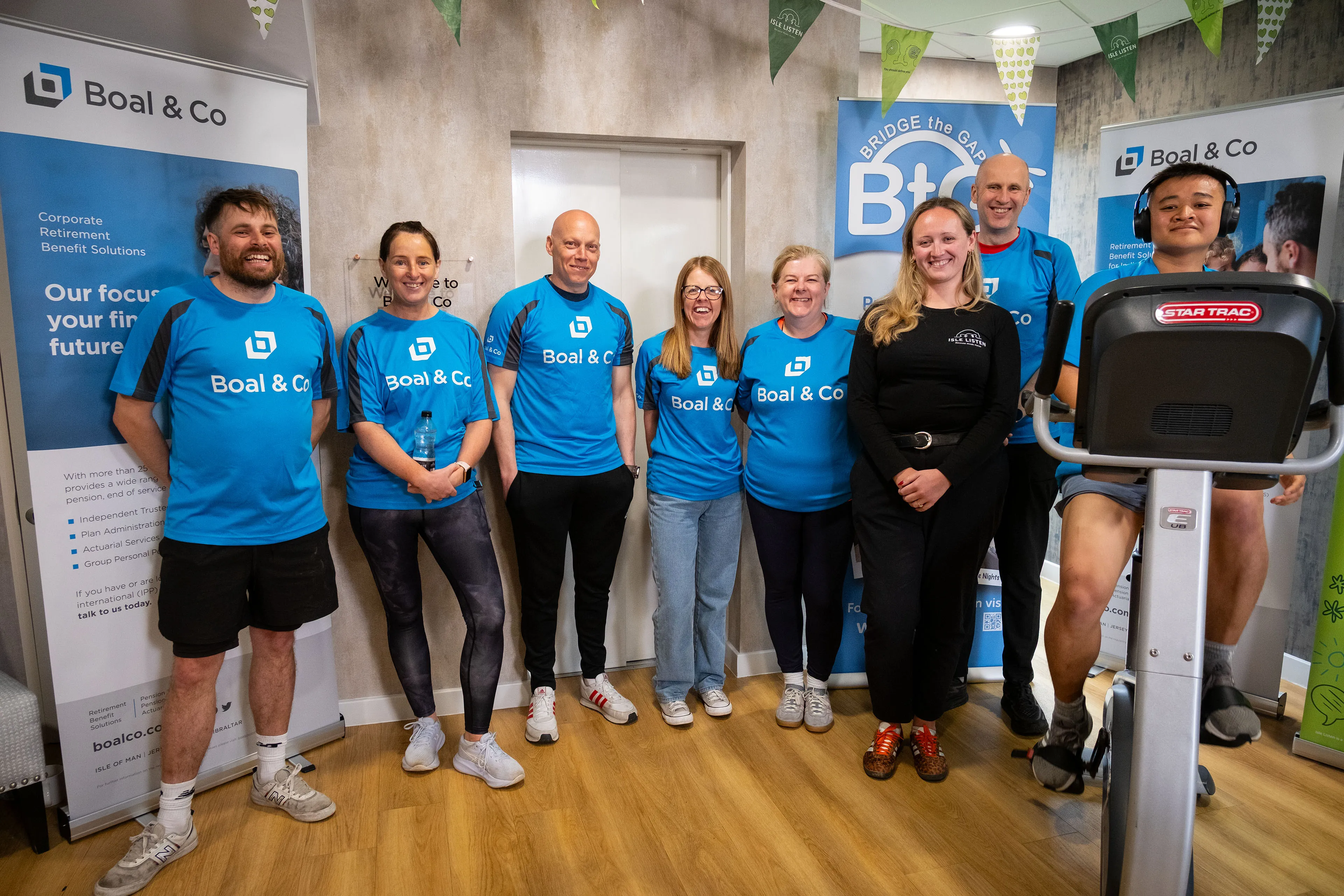 Andrew Cover, Karen McHale, Greg Collins, Vicky Mackie, Christine Evans, James Bassett and Joshua Zote in branded cycling jerseys with Jess Knight from Isle Listen, taken at the Boal & Co office on the Isle of Man during the charity cycling challenge