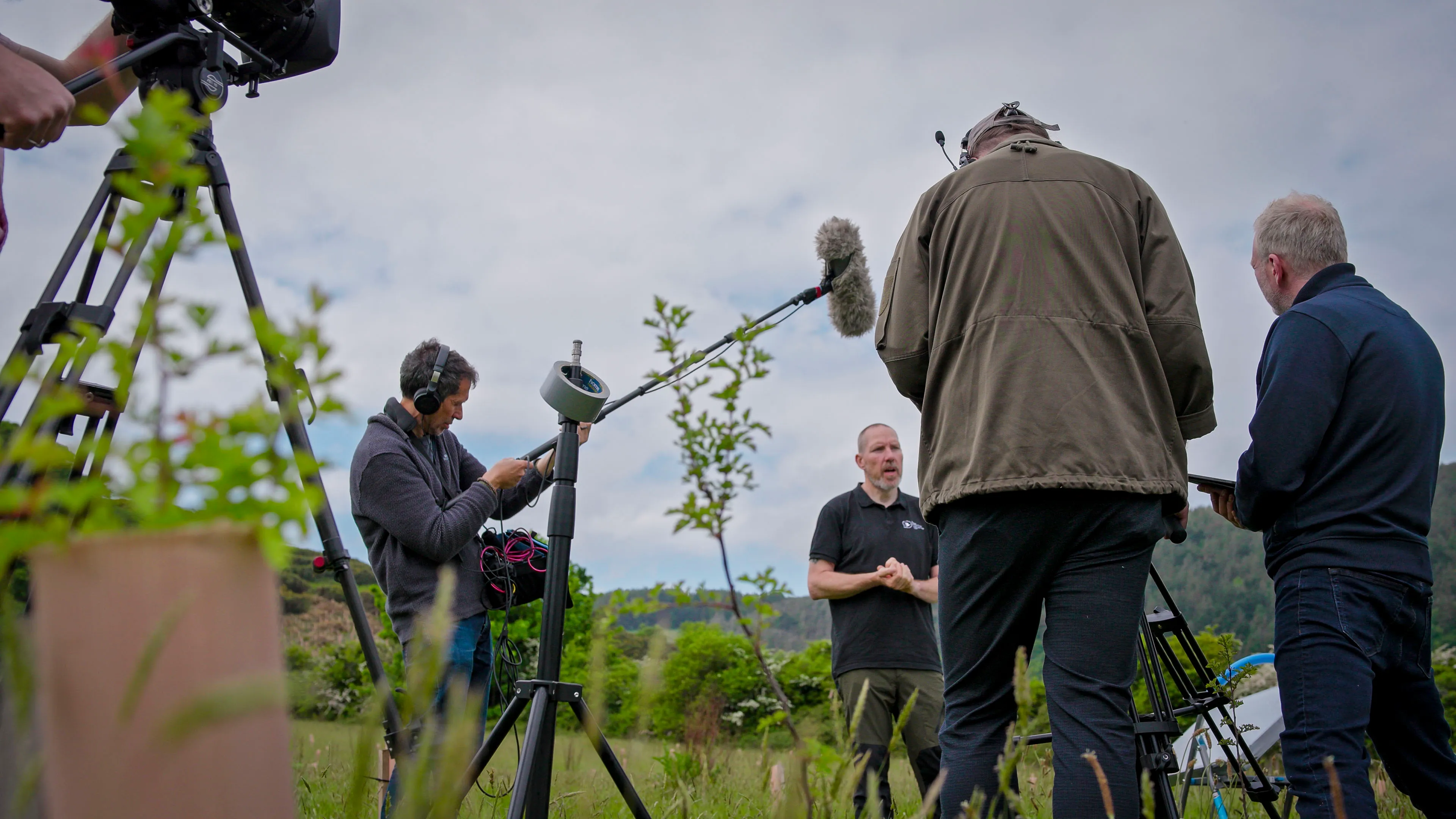 DotPerformance video production crew filming an outdoor interview with boom microphone and cinema camera, with a presenter speaking to camera in a natural landscape setting