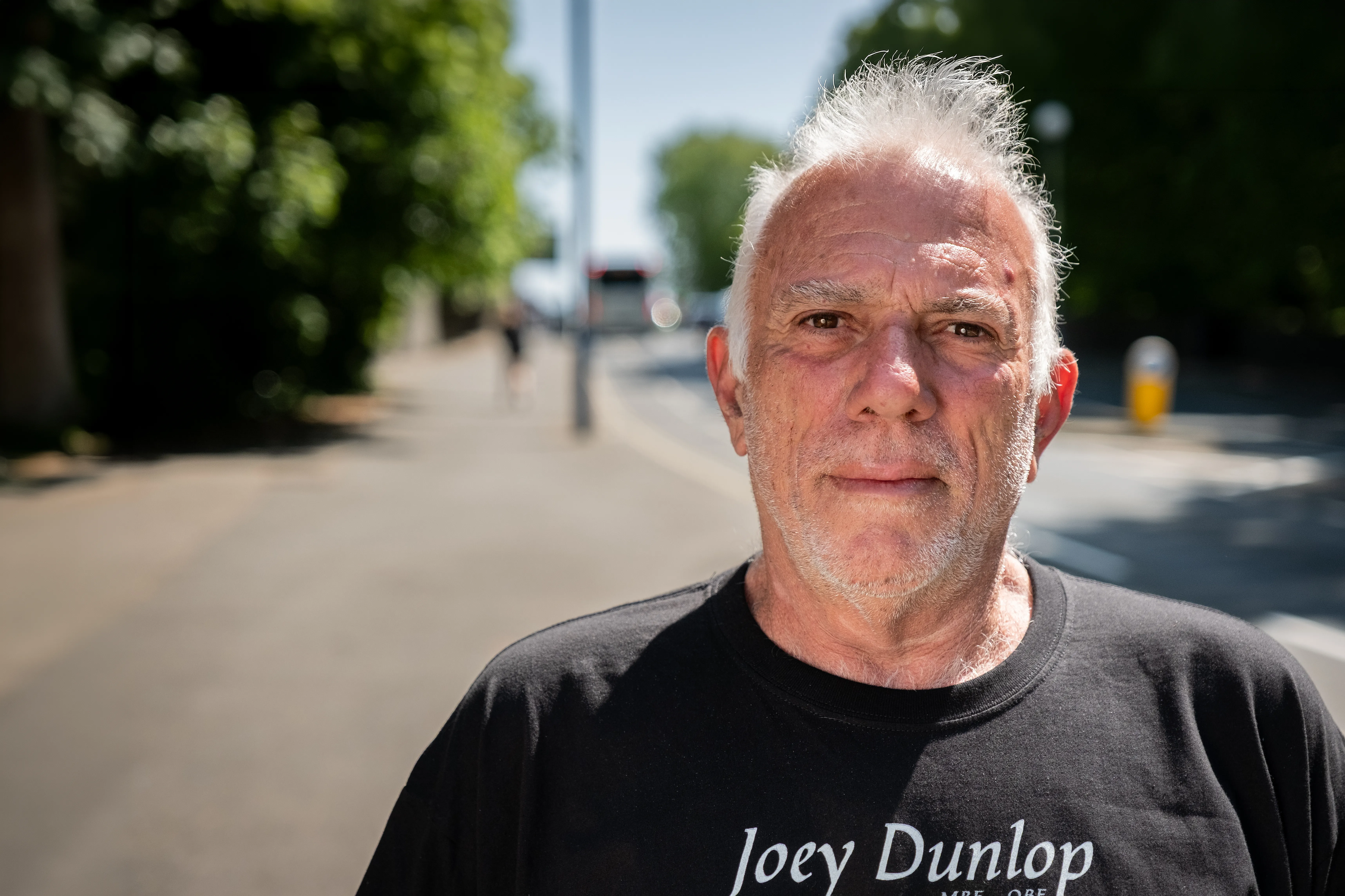 Marcelo Badano from Buenos Aires, Argentina, an Isle of Man TT Marshal, posing outdoors for Behind the Tabard TT Marshals Series, highlighting marshal stories, in a black Joey Dunlop t-shirt