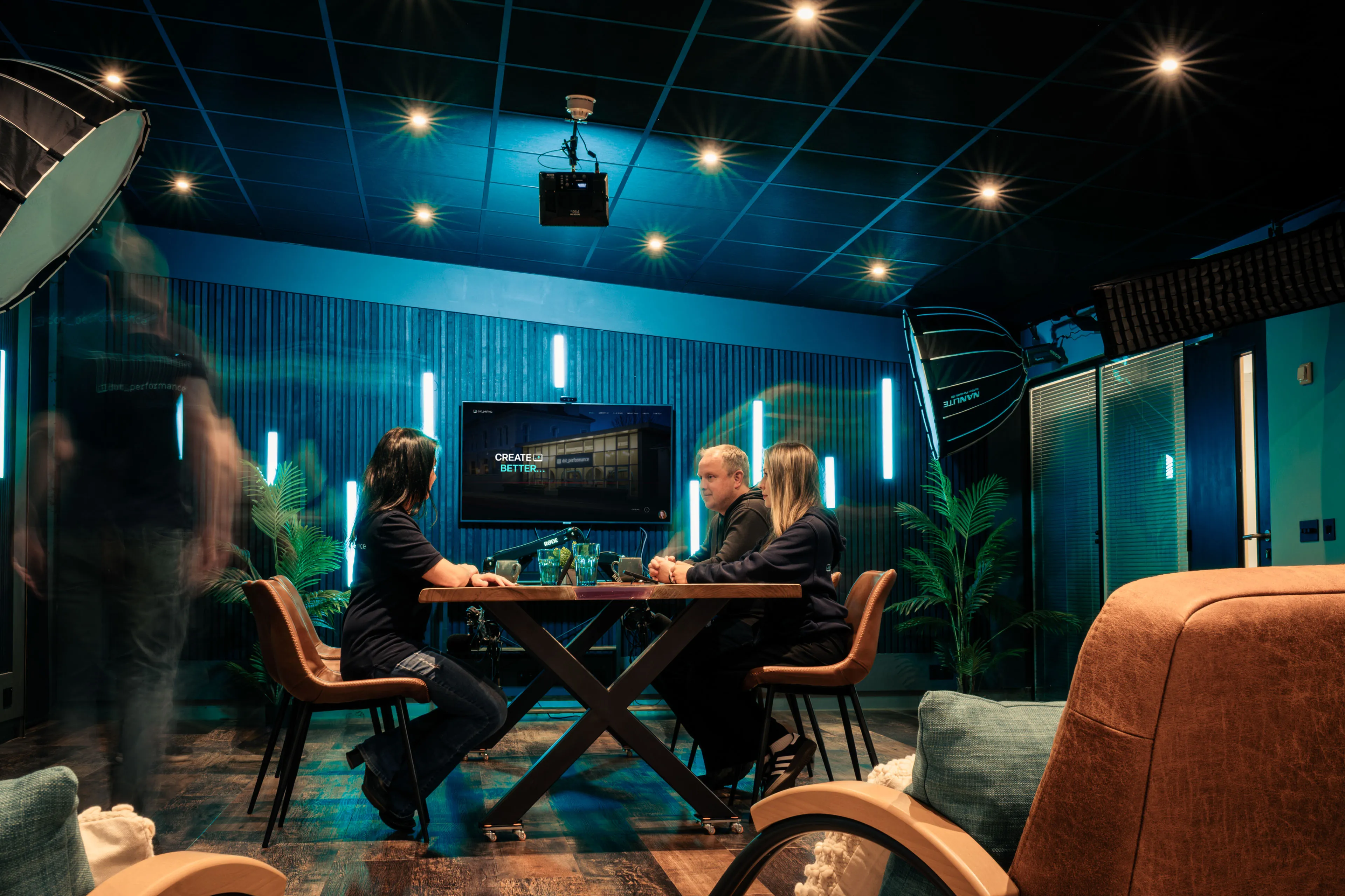 DotPerformance team with Juan Readshaw, Raluca Matei Orton and clients in a meeting at the Douglas studio, with Nanlite lighting rigs and a screen displaying the DotPerformance website visible in the background