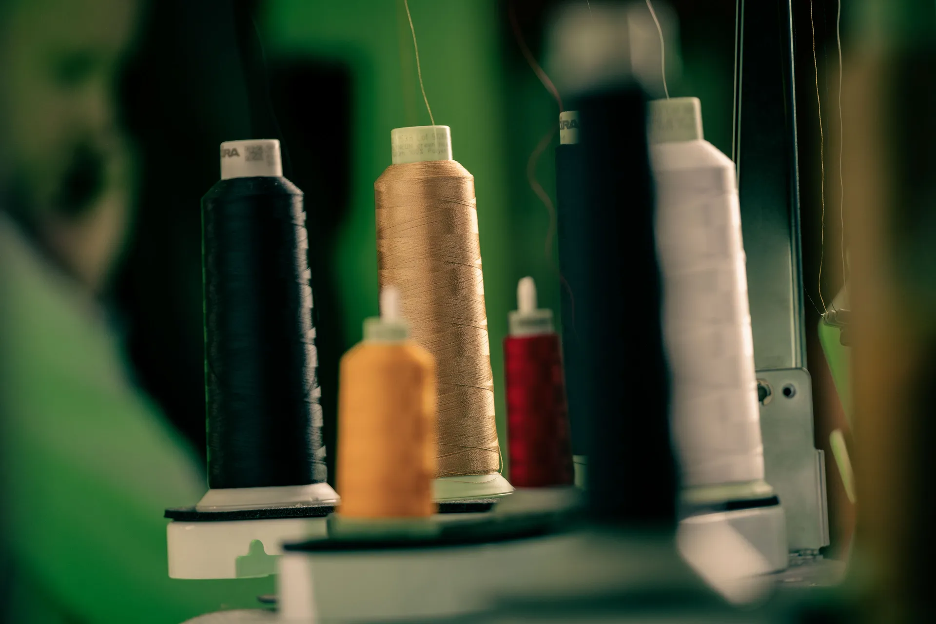 Close-up of sewing thread spools in various colors, including black, gold, and white, on a blurred green background, evoking creativity and craftsmanship.