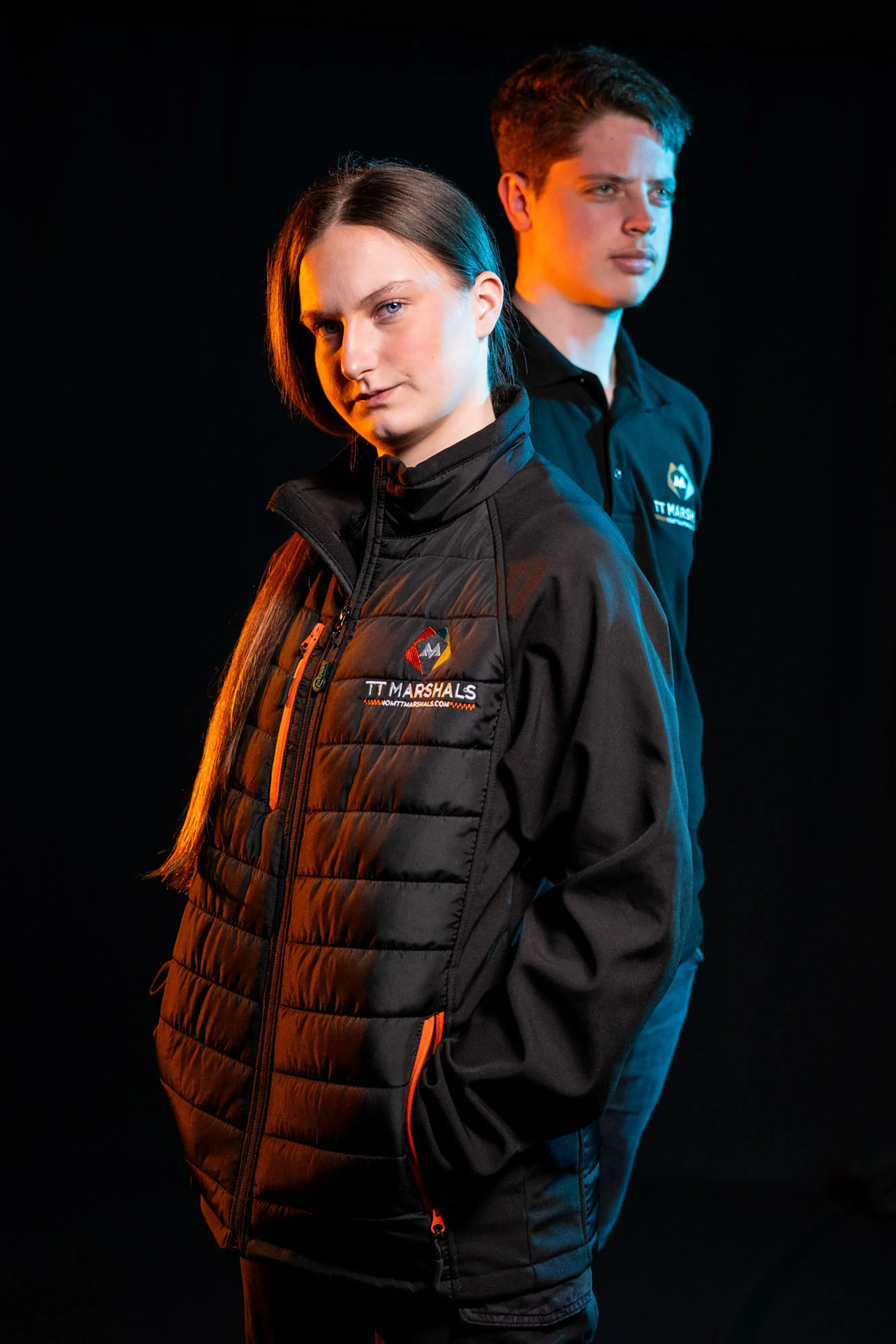 Caitlin Hampson and Deane Corlett Aspell wearing the official TT Marshals 2026 black polo shirt and softshell padded jacket, featuring the TT Marshals logo. Exclusive marshal merchandise for the Isle of Man TT 2026.