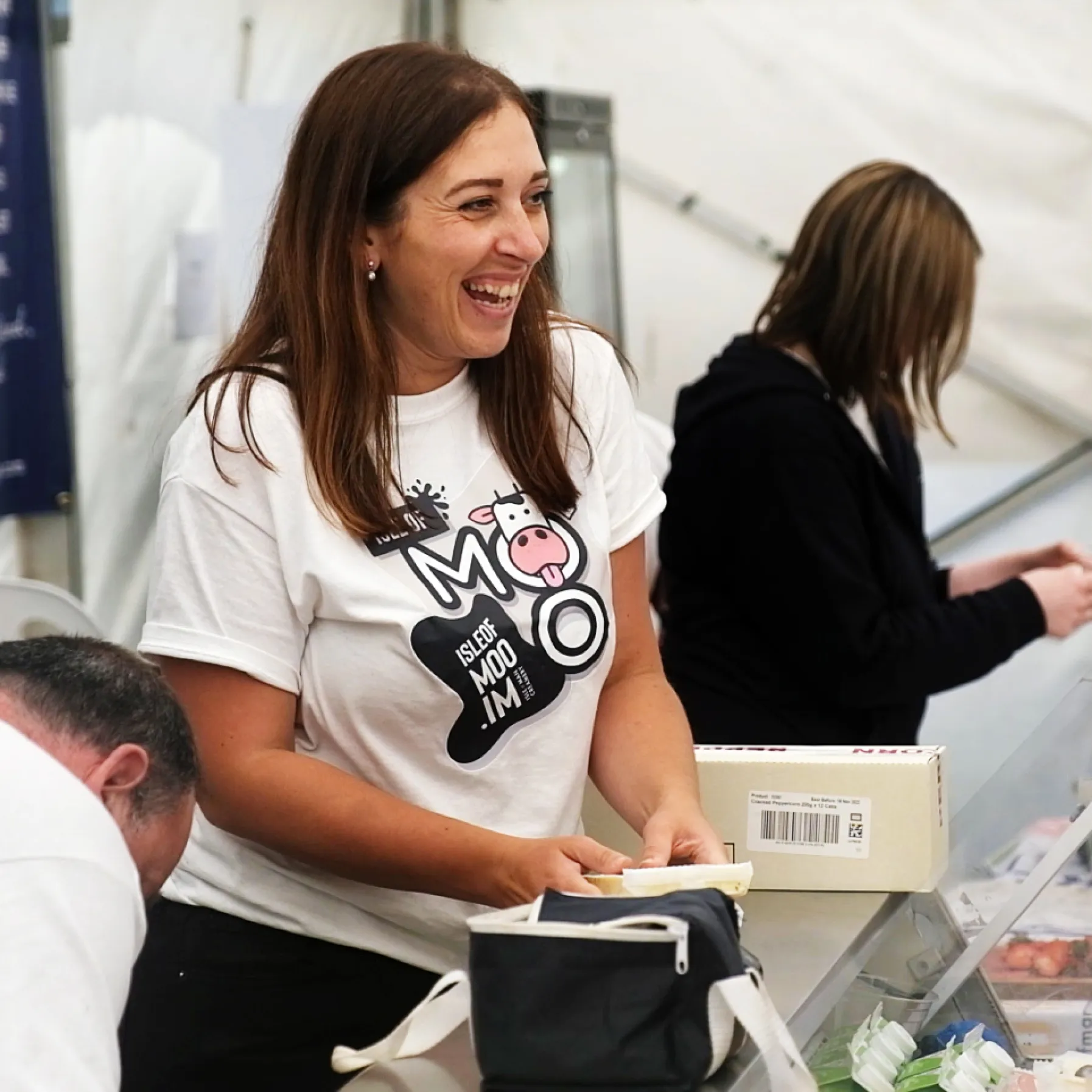 Woman wearing Isle of Moo branded t-shirt smiling while interacting with visitors at a promotional stand.